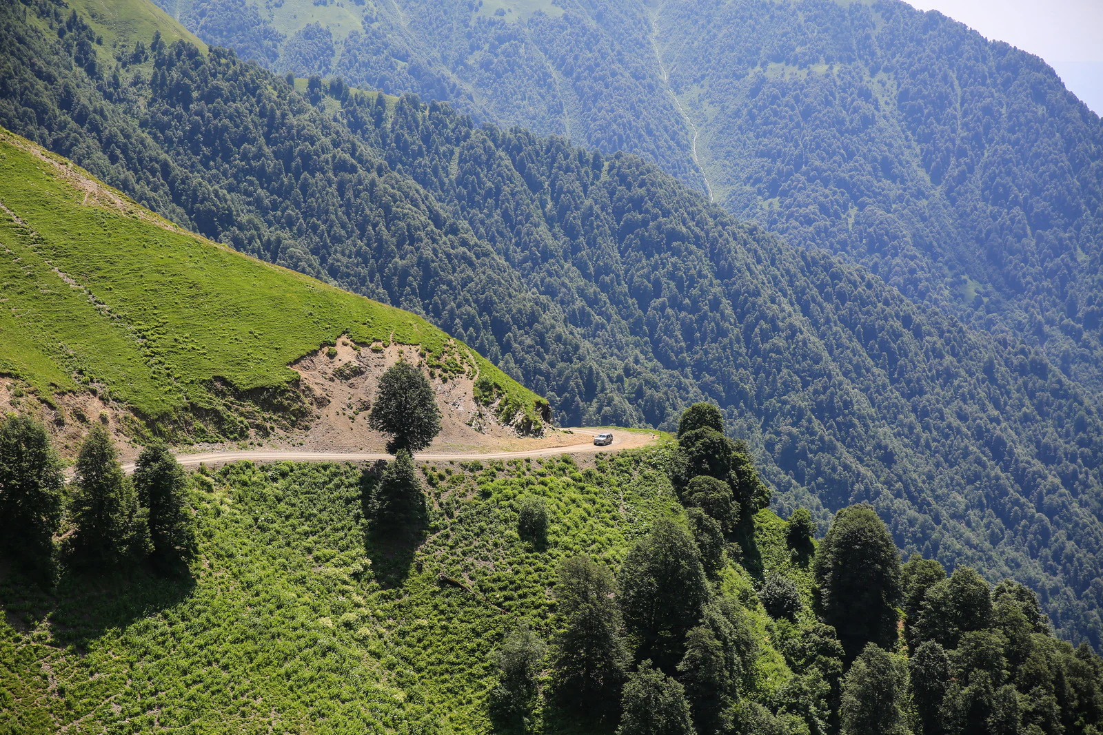 A mountain road winding through lush green hills and forests with steep mountain slopes rising in the background