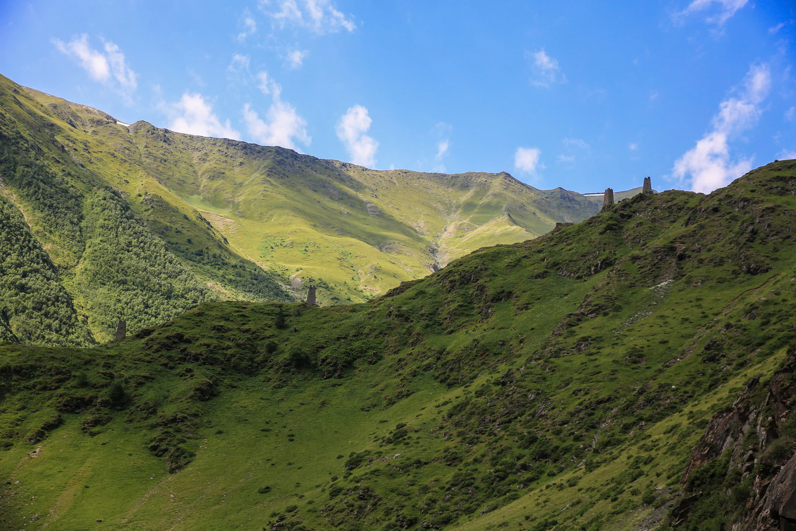 A wide view of green mountainous terrain with valleys under a blue sky with scattered clouds