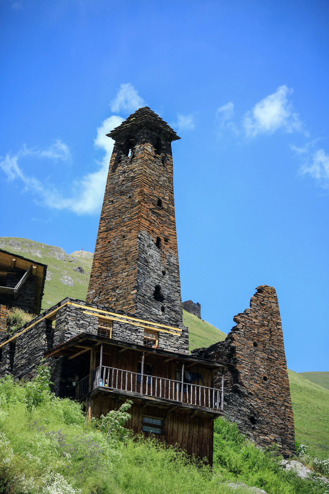 Stone tower with wooden balcony, surrounded by green hills and blue sky