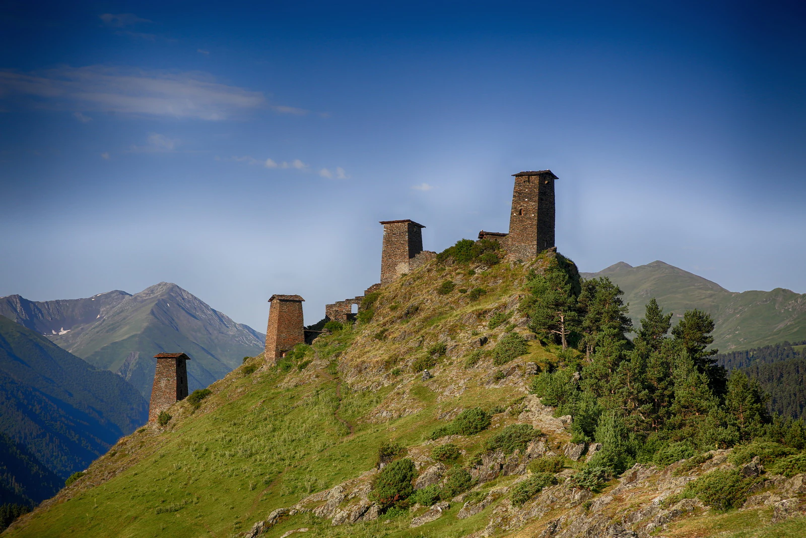 Stone towers on a grassy hilltop with mountains in the background under a clear blue sky