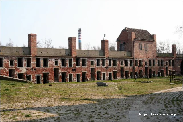 A long, two-story red brick building with multiple chimneys and arched openings surrounding a grassy courtyard at a historic fortress.