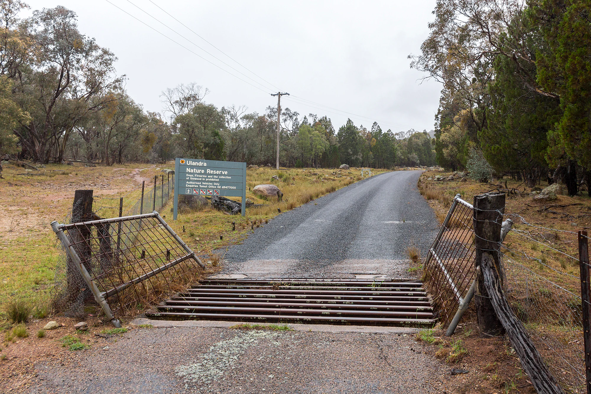 A gravel road leads into Ulandra Nature Reserve, passing through an open metal cattle grid with a green park information sign visible on the left.