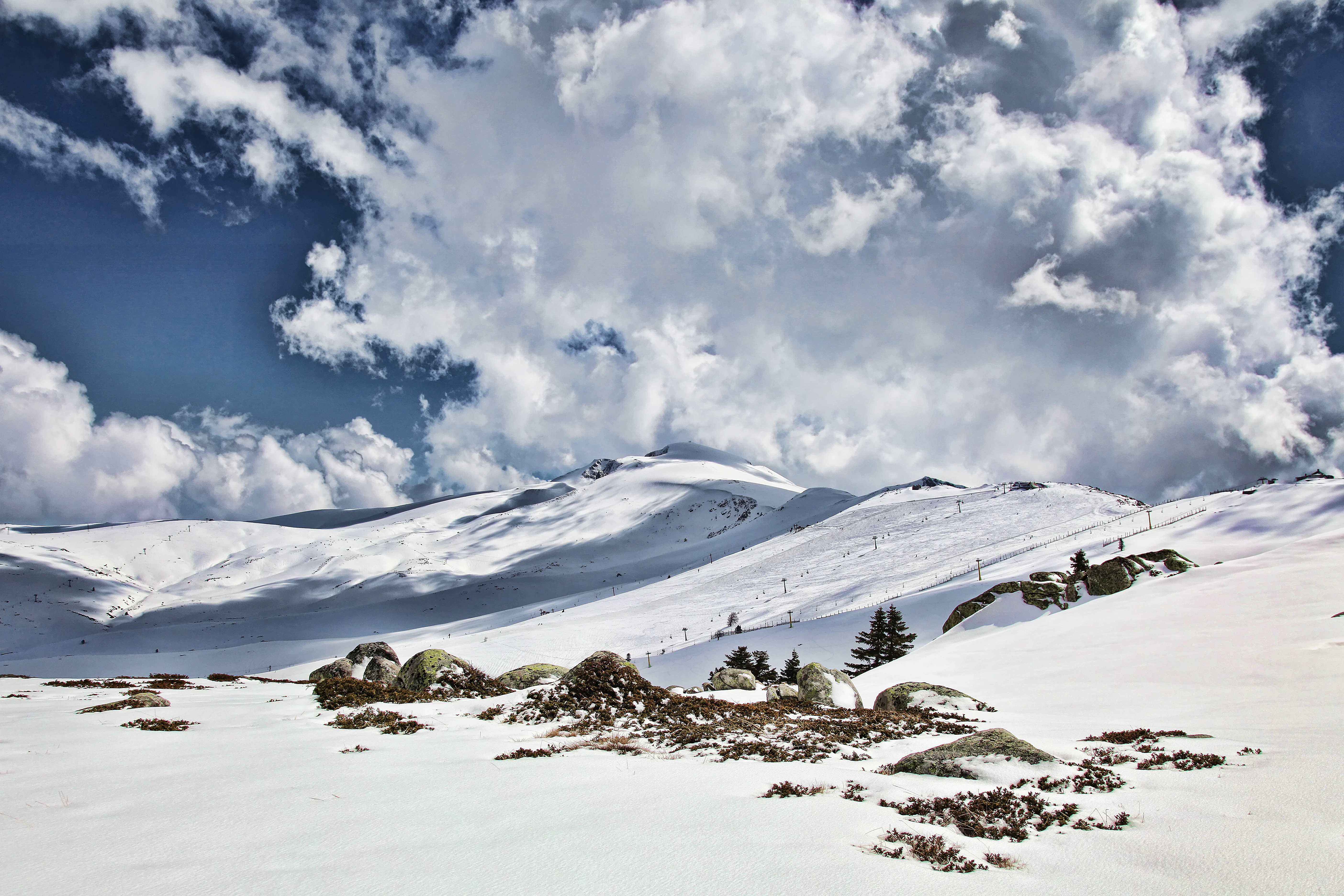 Snow-covered mountain landscape with patches of exposed ground and scattered rocks under a partly cloudy sky