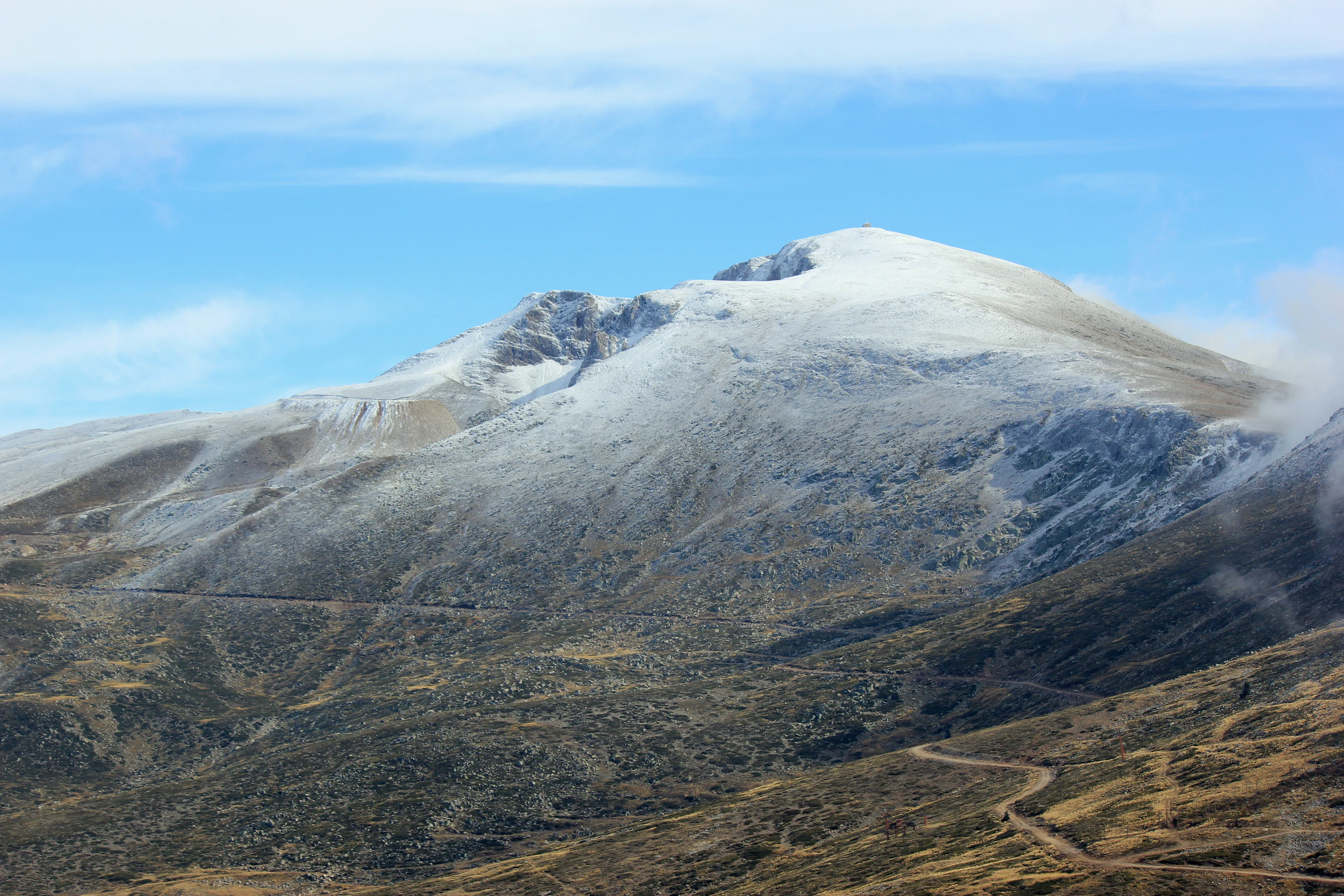 Snow-covered mountain peak with rocky slopes visible under partly cloudy sky