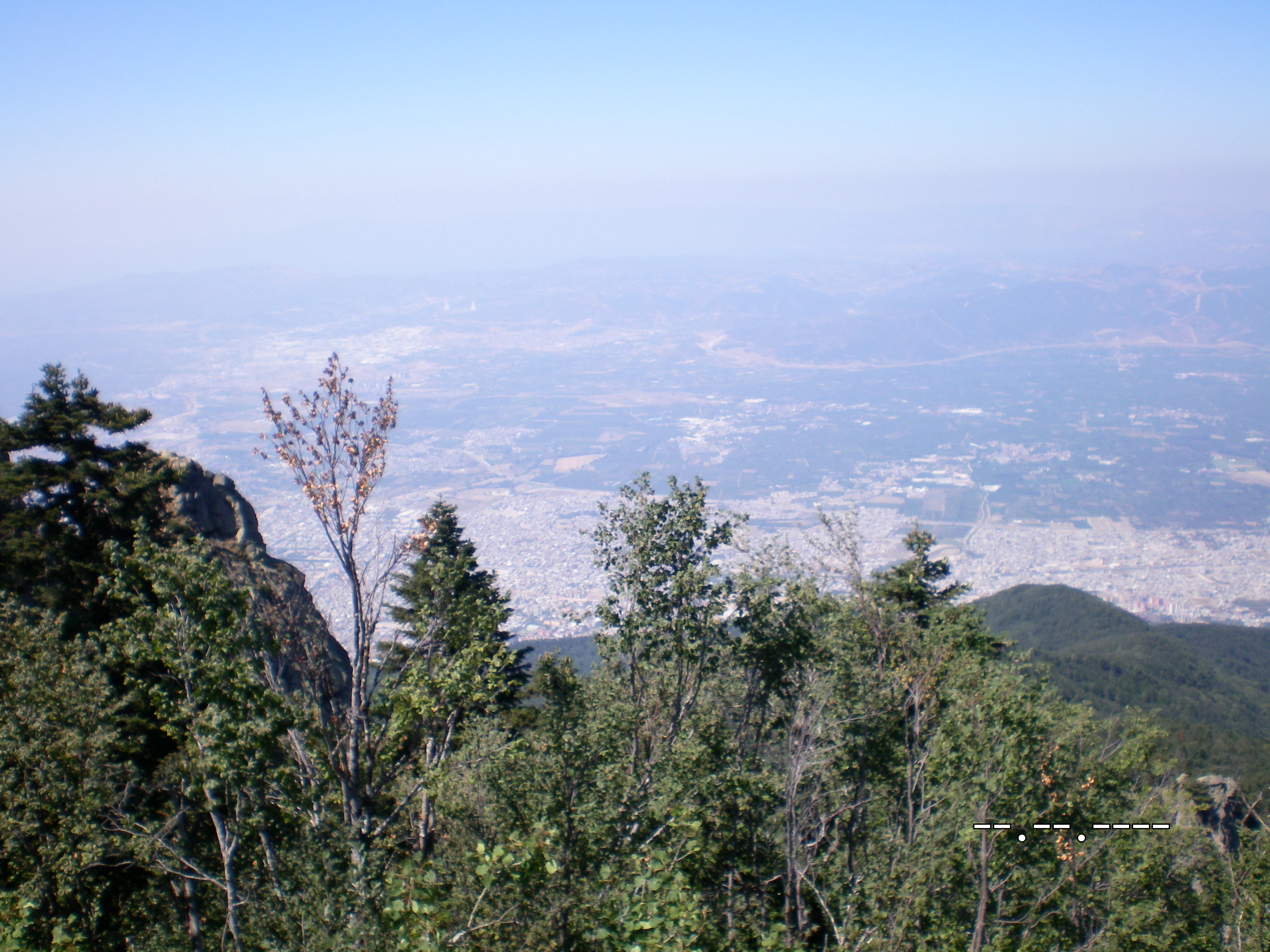 Panoramic view from Bakacak viewpoint showing forested hills, distant cityscape, and hazy valley under clear blue sky