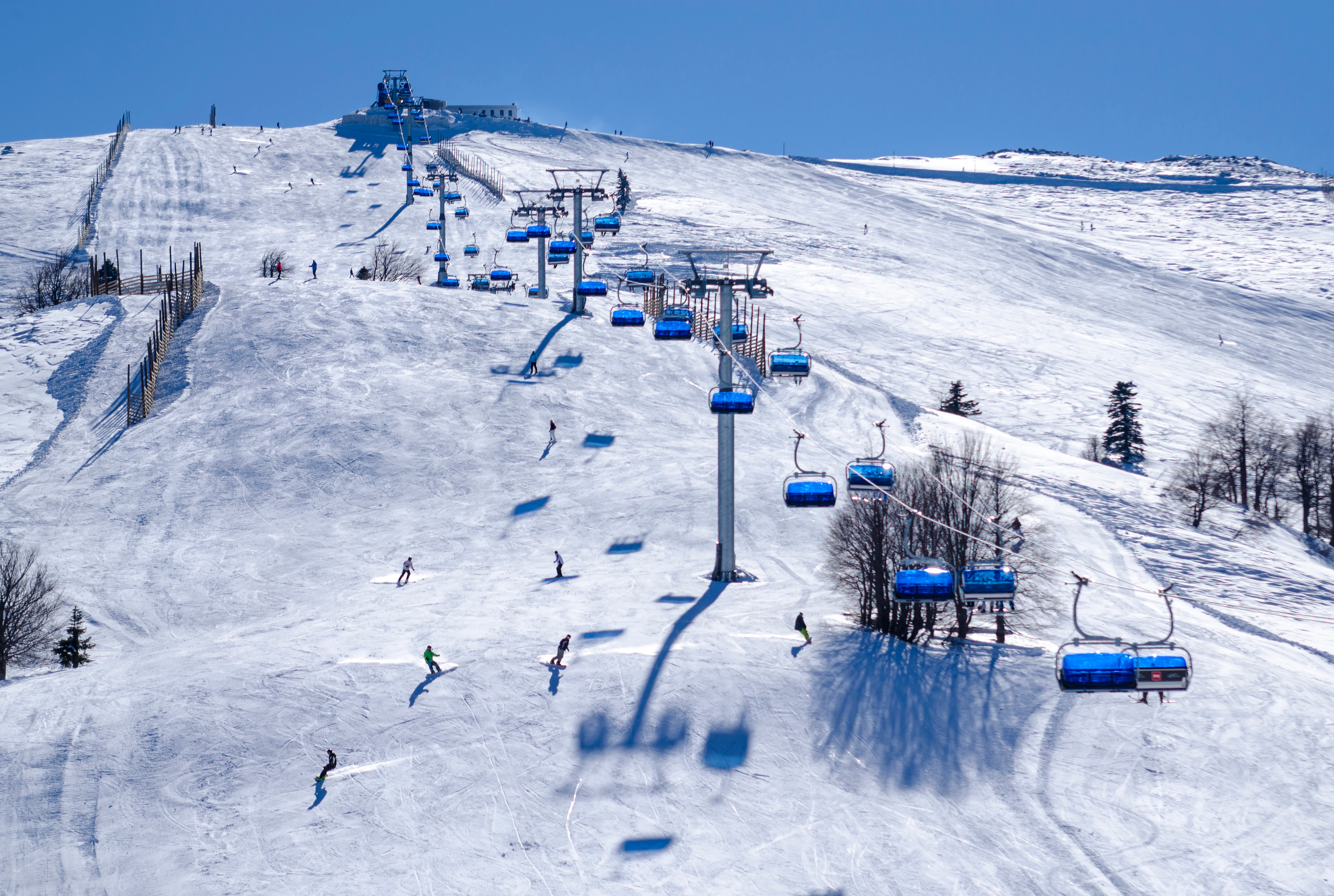 Snowy mountain slope with blue ski lifts and multiple skiers on a clear day