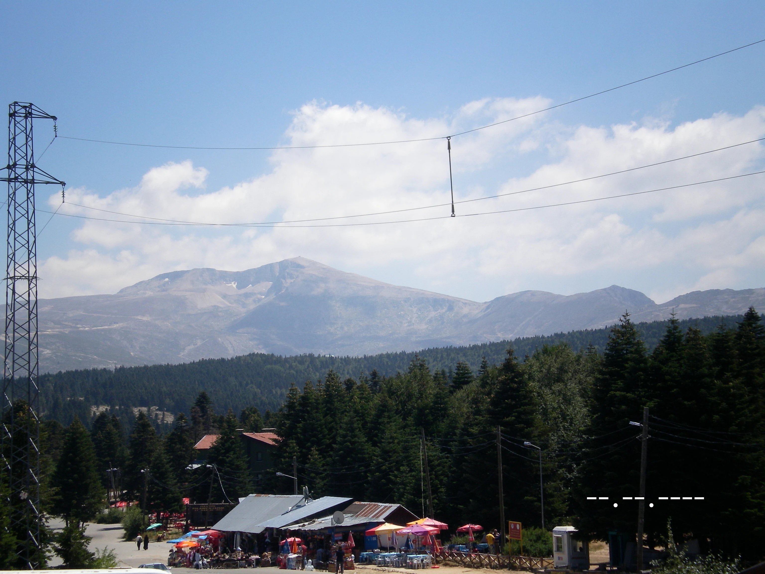 View of Mount Uludağ mountains, forested hills, and a small settlement with buildings under a partly cloudy sky