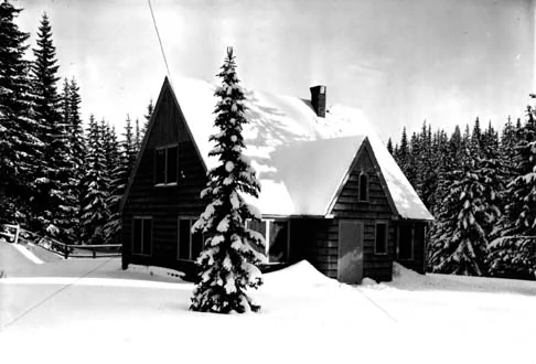 A black and white archival photograph of a gabled, wooden ranger station residence surrounded by snow and conifer trees in 1935.