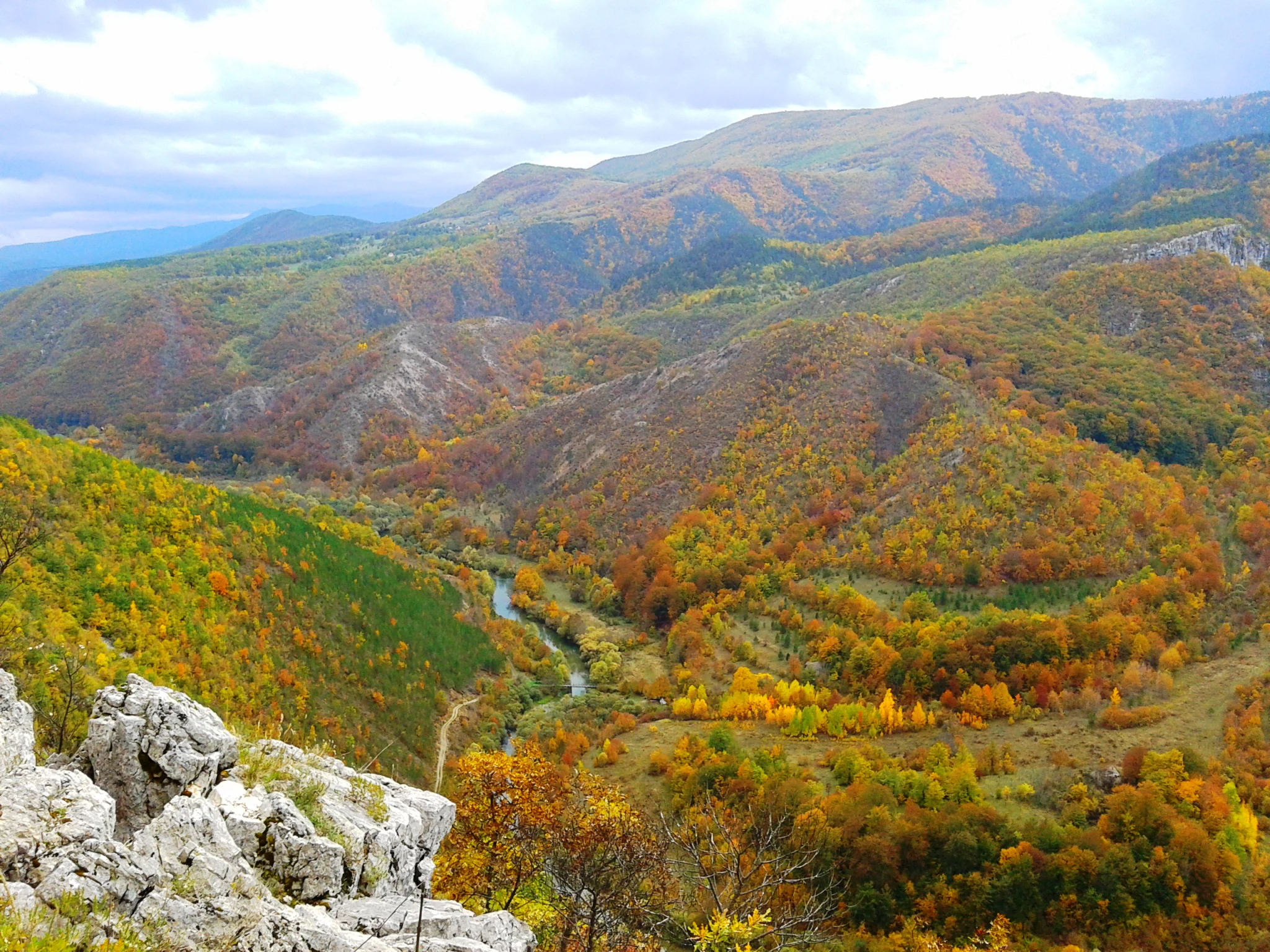 Wide landscape view of Una National Park featuring a river winding through a canyon with autumn-colored trees and rocky outcrops