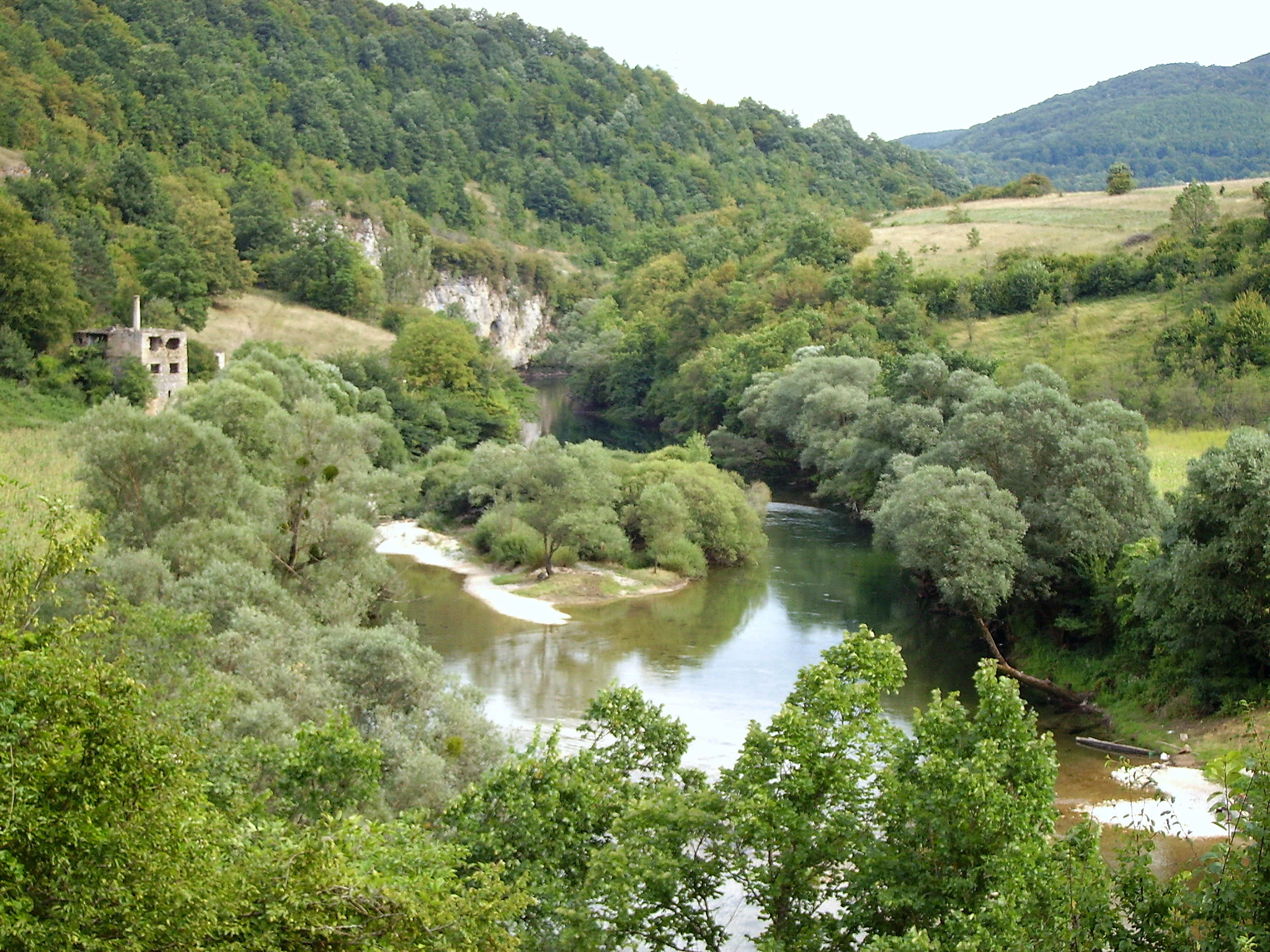 River Una flowing through a verdant valley surrounded by dense forests and hills with a small ruined building visible on the left hillside