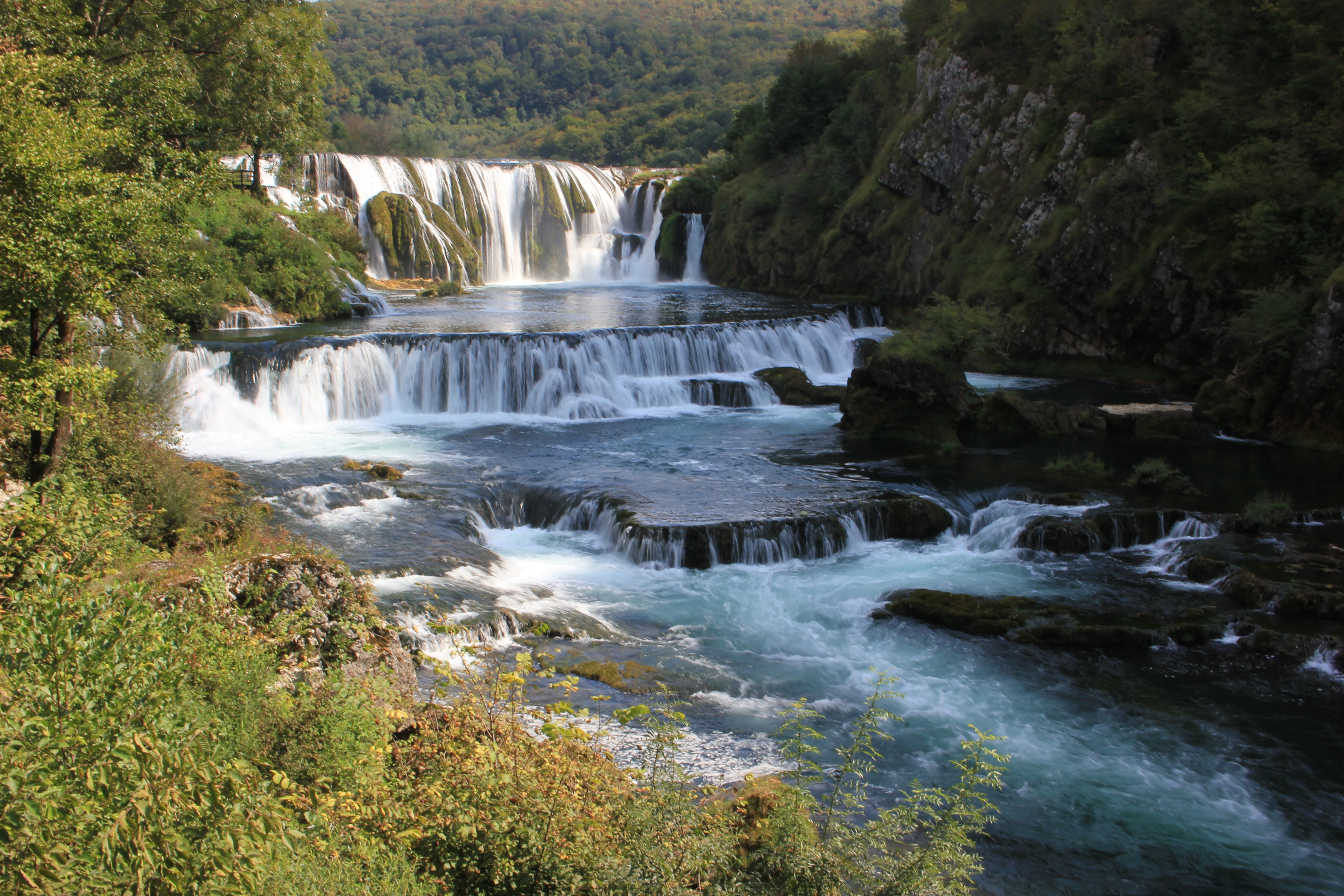 Multi-tiered waterfall flowing into a river surrounded by green vegetation and rocky cliffs