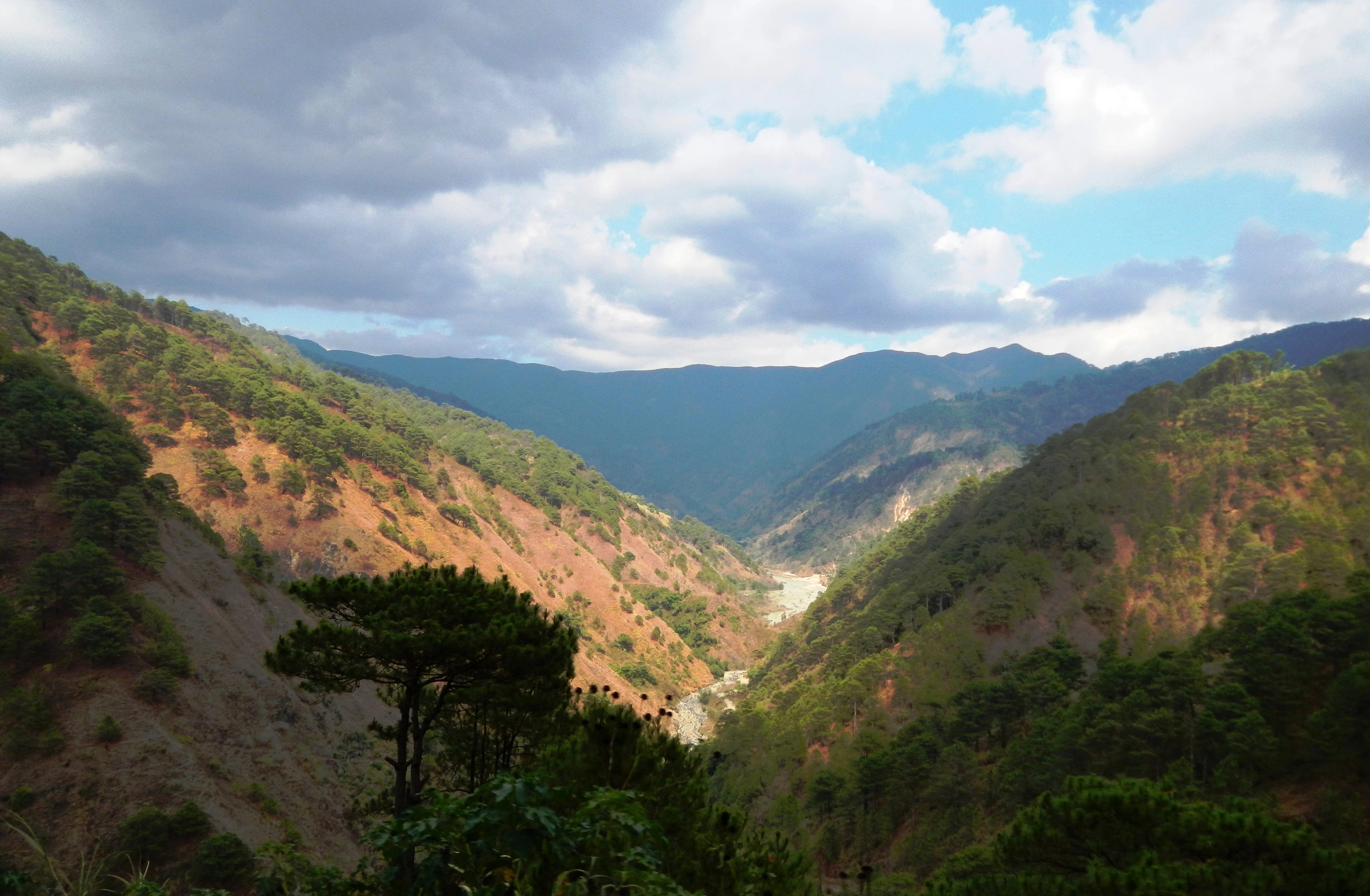Wide angle view of forested mountain slopes and deep valleys under a cloudy sky in the Philippines.