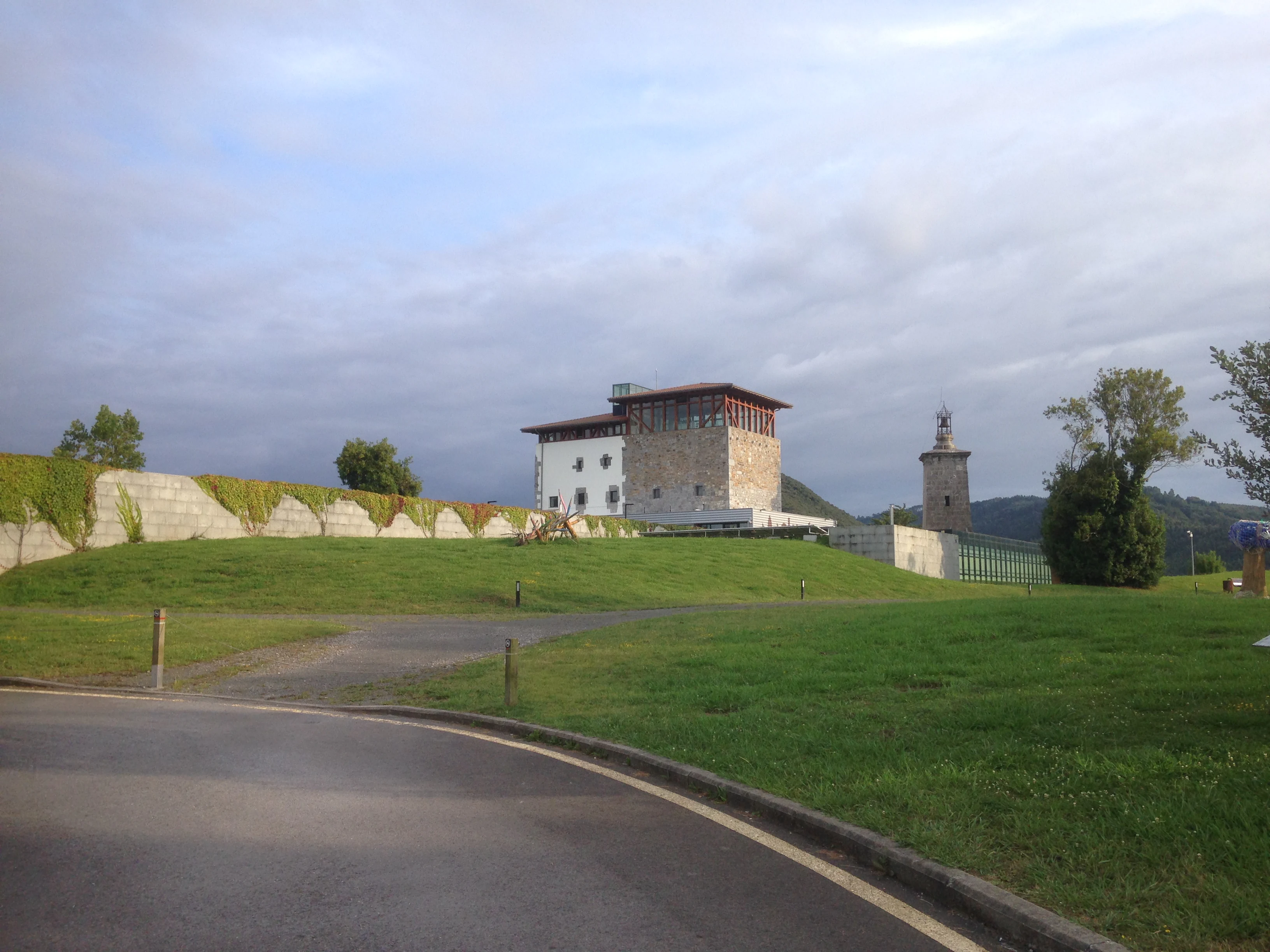 A historic stone tower building surrounded by green lawns and a stone wall under a cloudy sky.