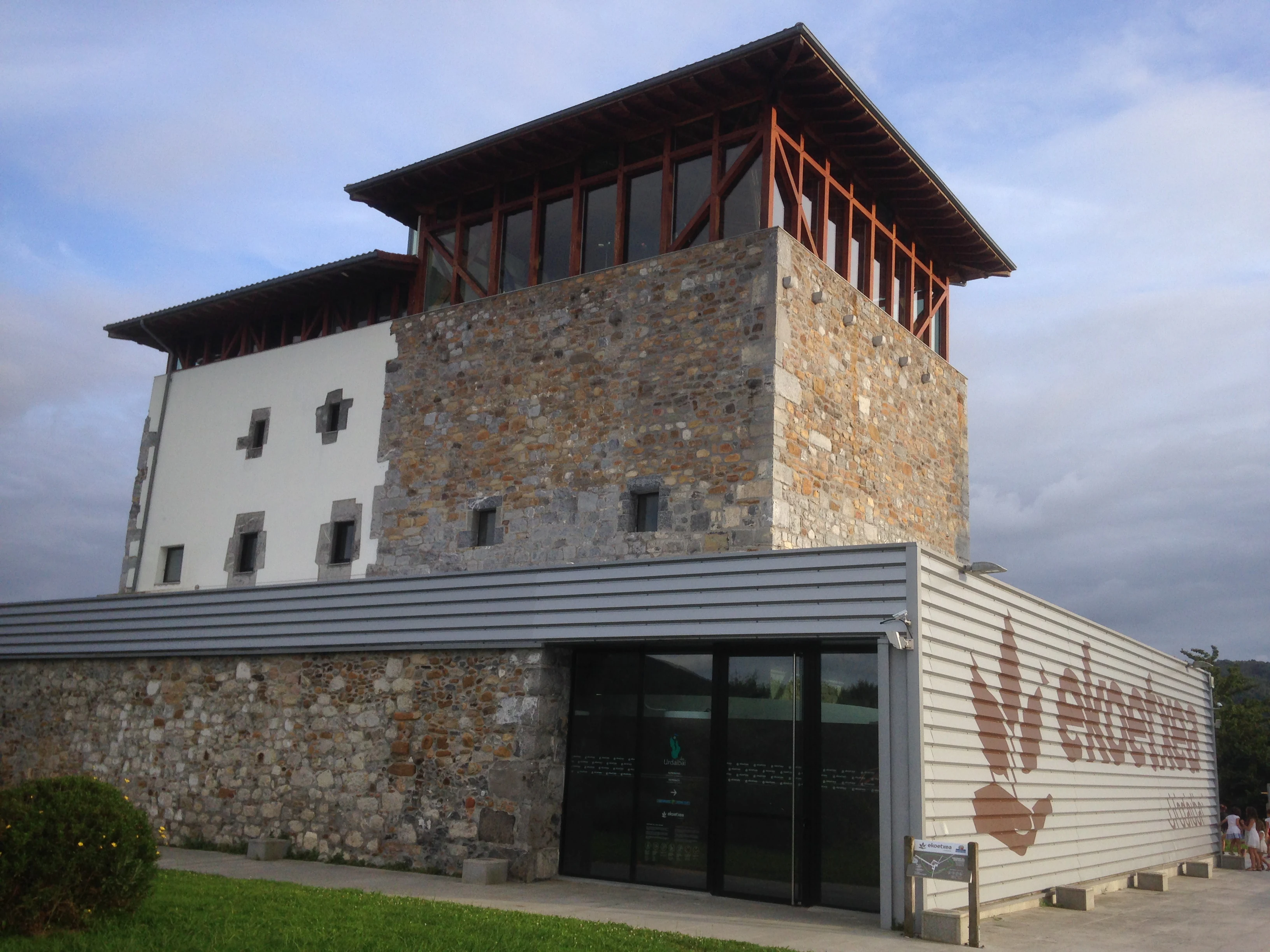 The Ekoetxea Urdaibai visitor center in Busturia, featuring a stone tower with a wooden gallery attached to a modern, single-story metal-clad building.