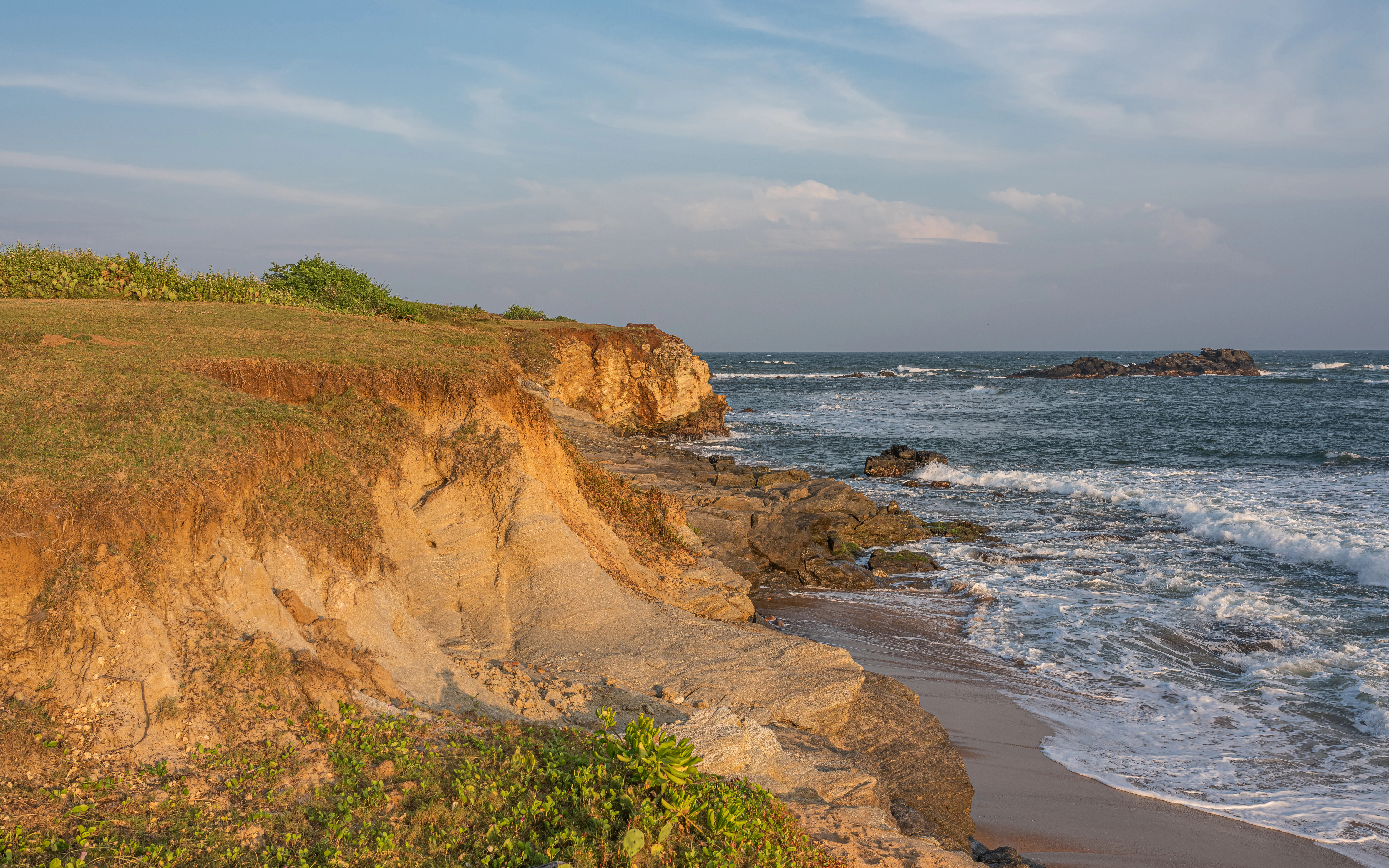 Coastal cliffs with sandy beach and ocean waves under partly cloudy sky