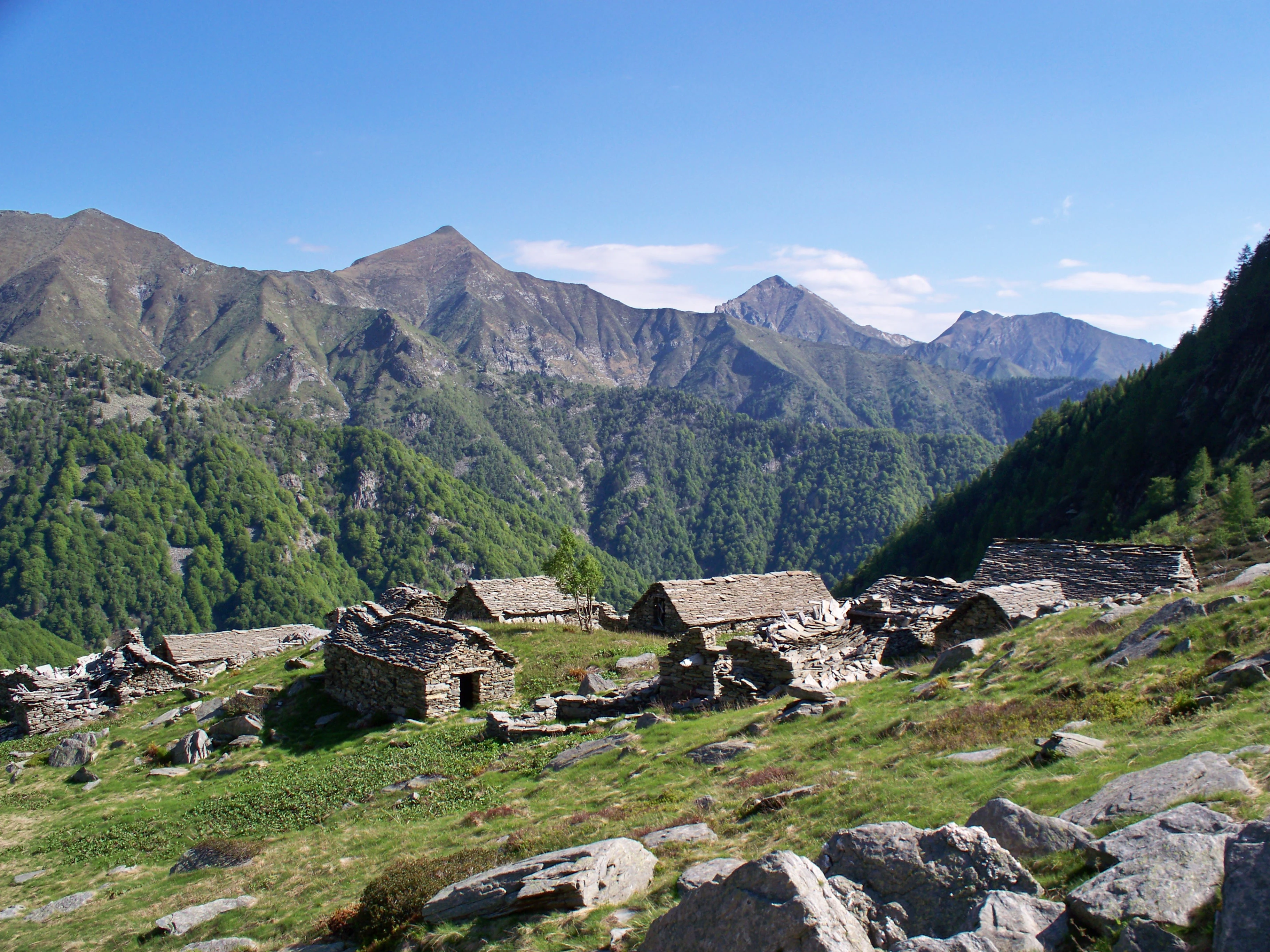Abandoned stone farmhouses on a grassy hillside, mountain peaks in background