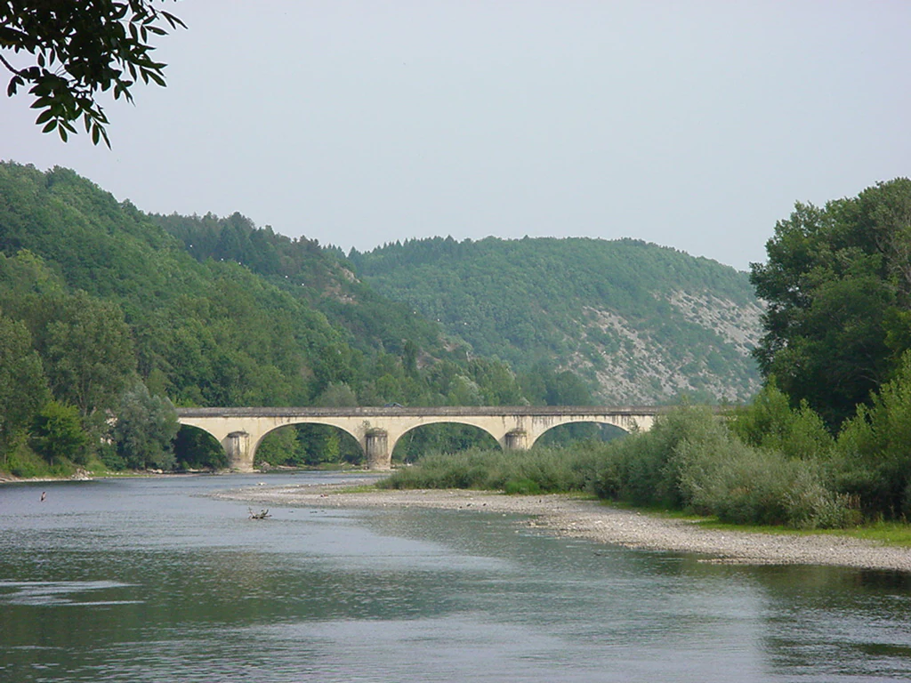 A wide shot of a multi-arched stone bridge crossing a calm river with wooded hills in the background.