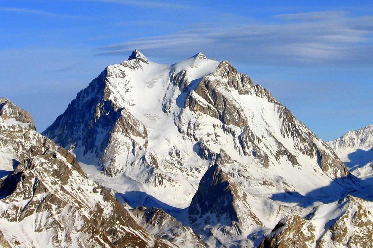 Snow-covered mountain peak with rocky outcrops under a blue sky with light clouds.