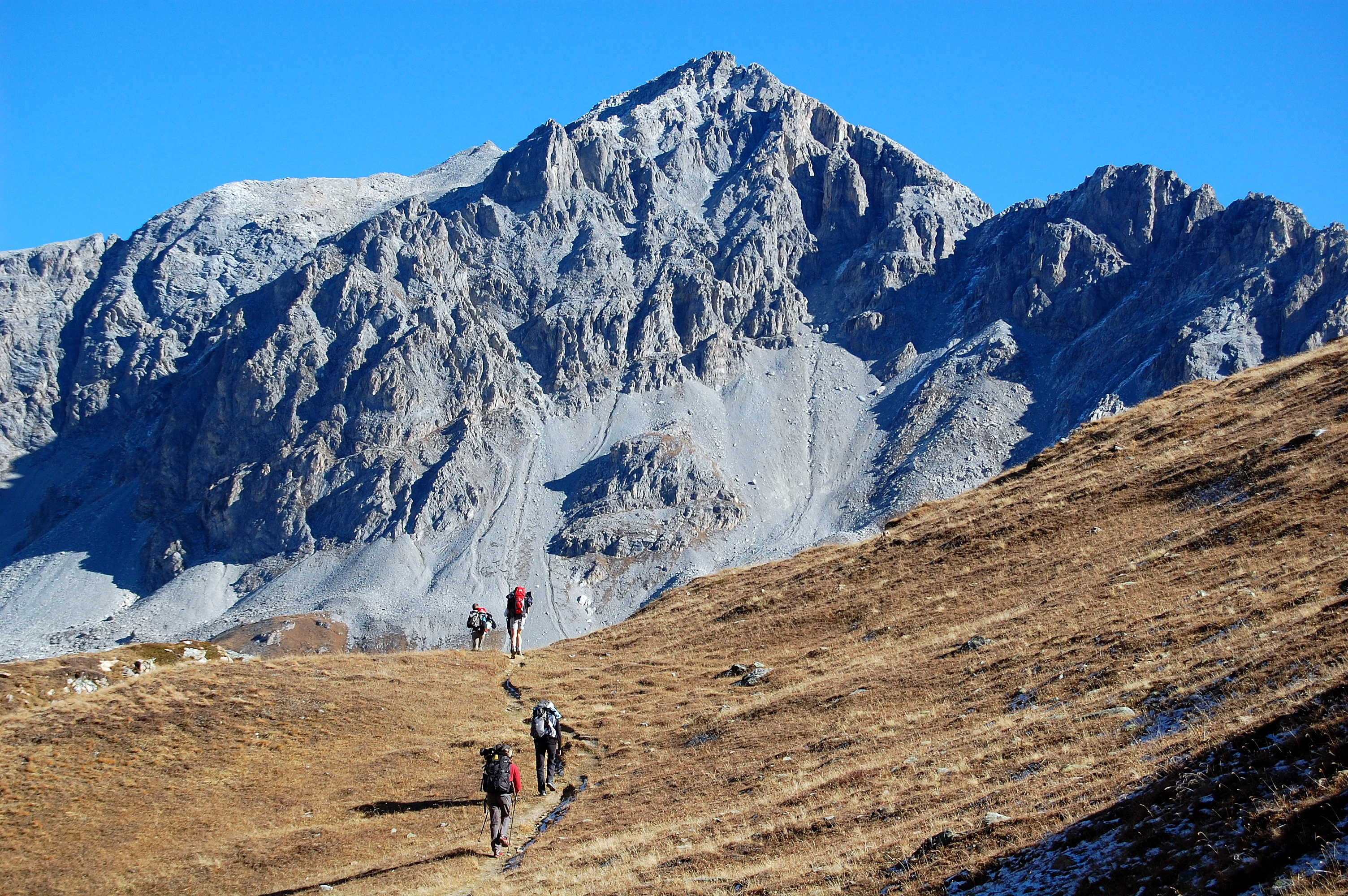 Hikers walking on a trail through a mountainous landscape with rocky peaks under clear blue sky
