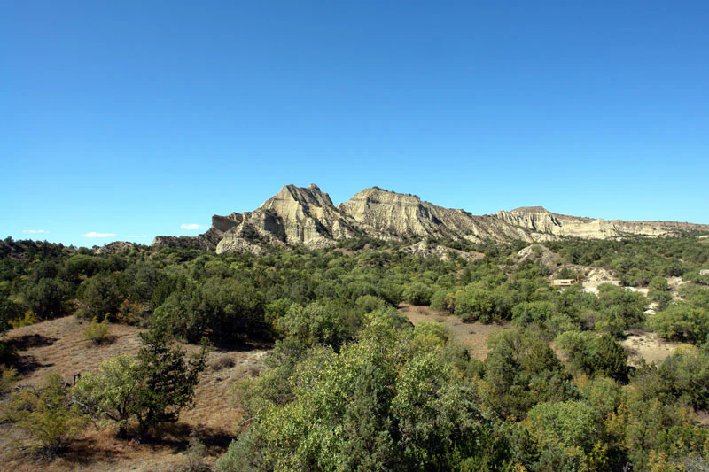 Wide view of rocky hill formations with scattered trees and clear blue sky in Vashlovani National Park