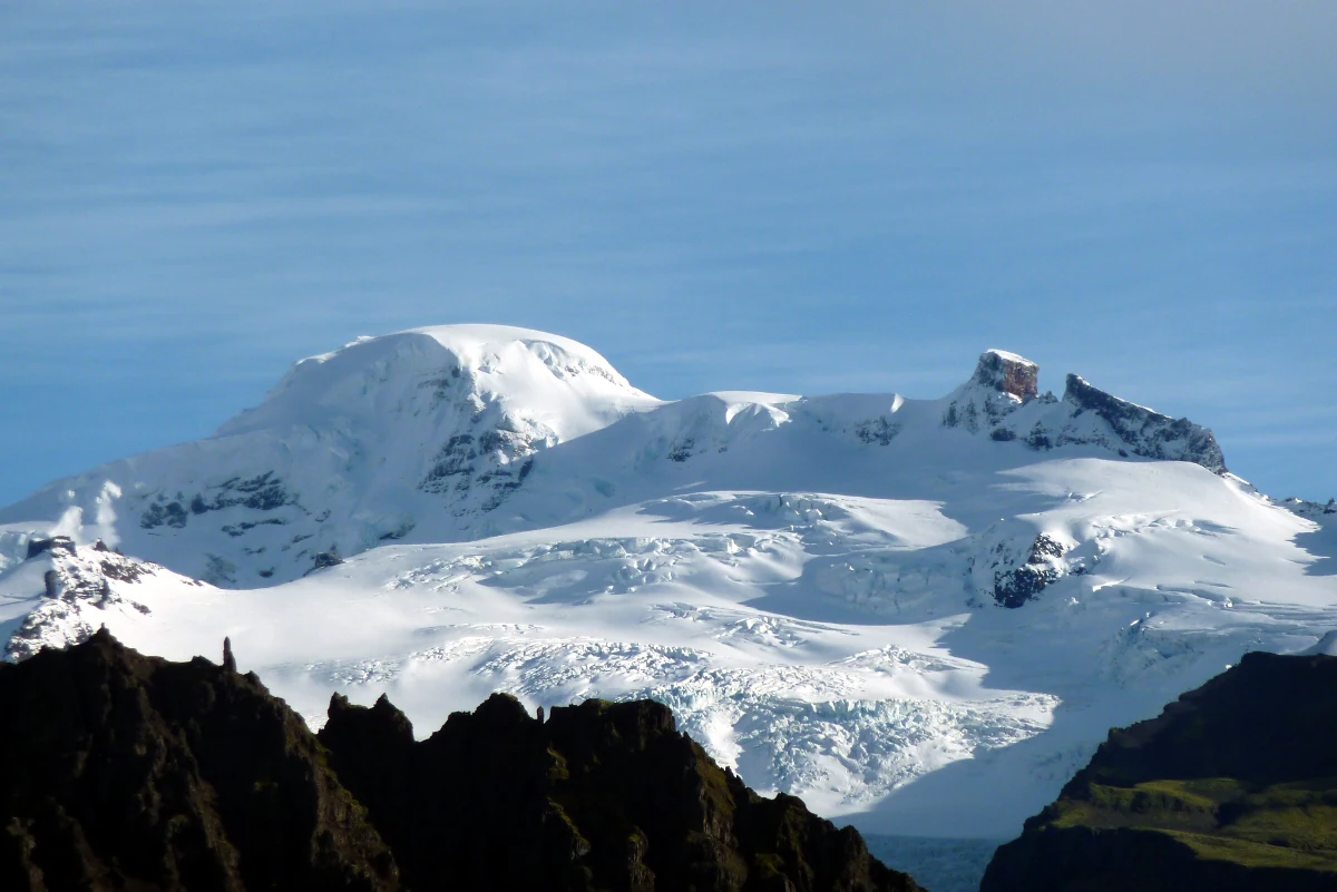 Snow-covered mountain glacier with rocky foreground under clear blue sky