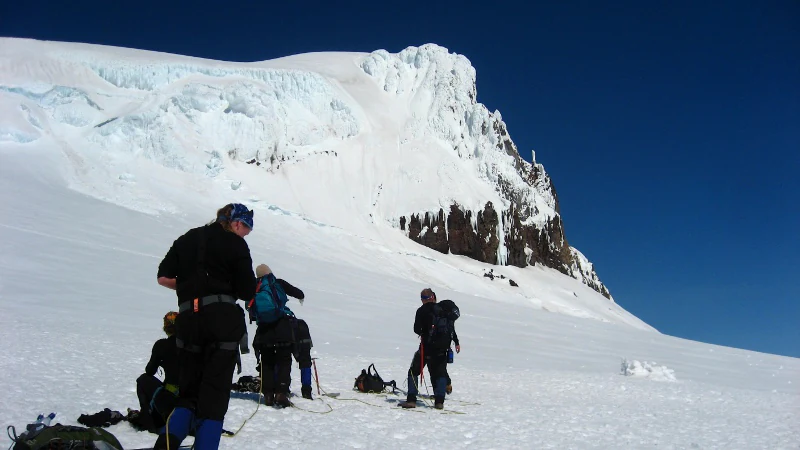 Group of climbers on snow-covered glacier with a large icy mountain peak under clear blue sky