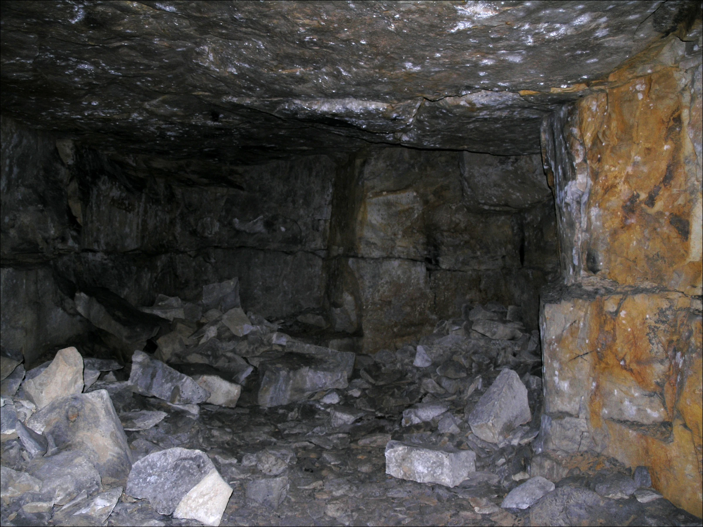 A view inside a dark, underground stone chamber with stacked opuka blocks and loose rock debris on the floor.