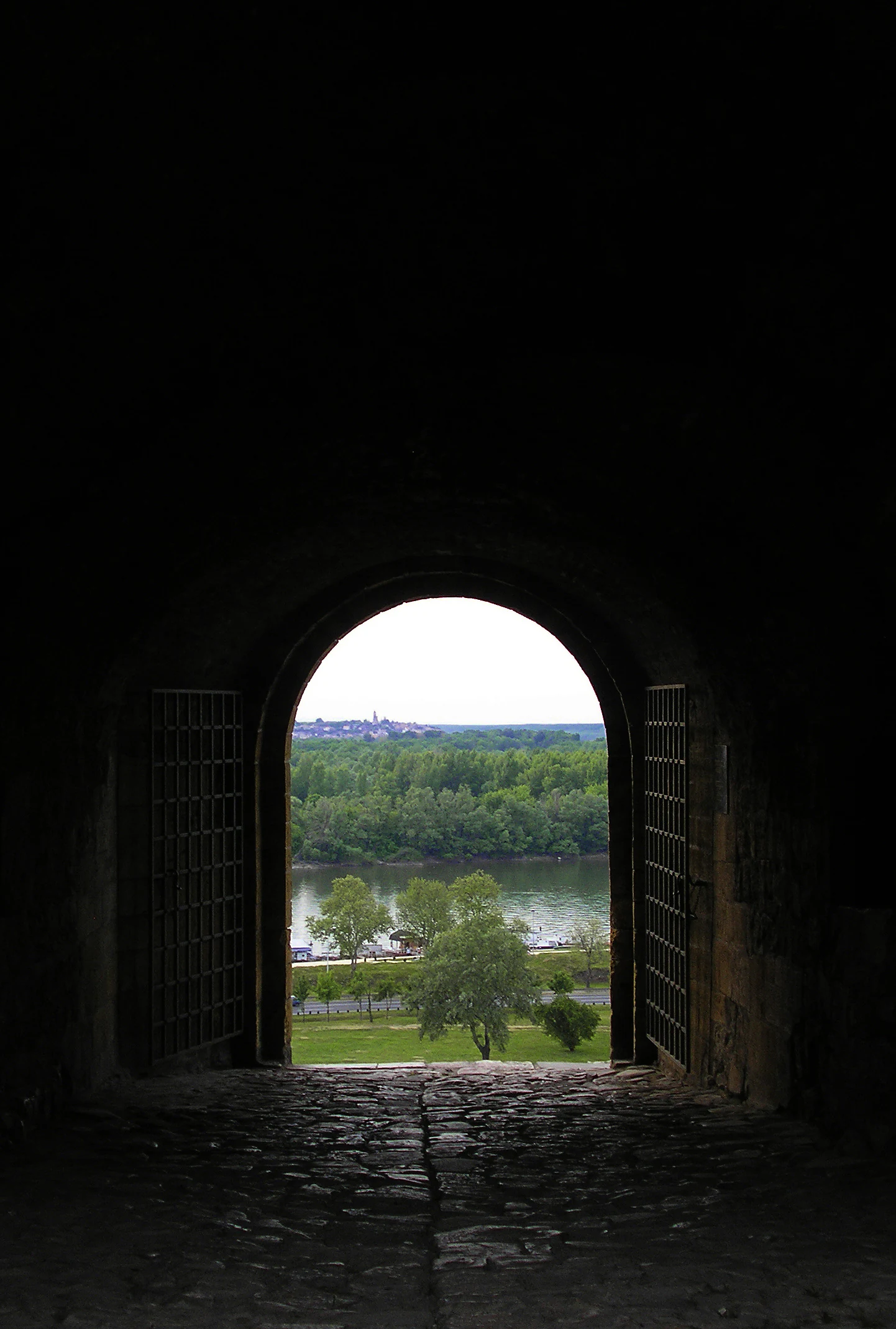 Stone archway with metal grilles framing a view of a forested island across a river