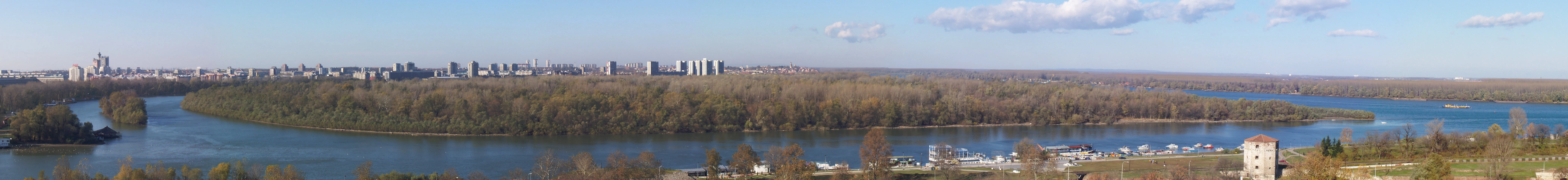 Wide river with islands covered in trees, distant city skyline under clear blue sky
