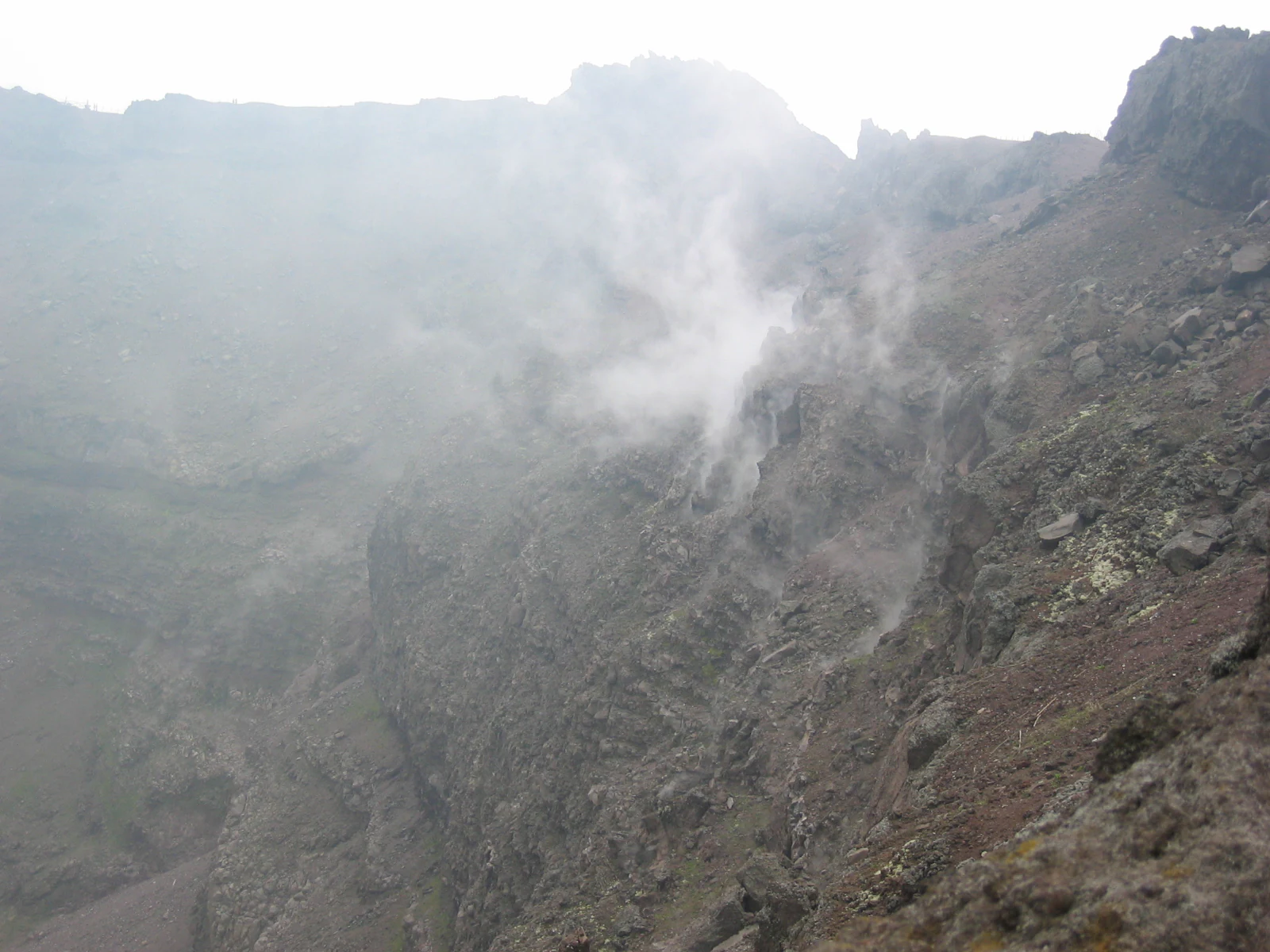 A misty volcanic landscape with rocky terrain and clouds surrounding Mount Vesuvius