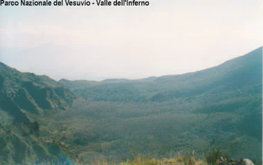 Wide view of a mountainous valley with green terrain and distant peaks. Text overlay reads 'Parco Nazionale del Vesuvio - Valle dell'Inferno'.
