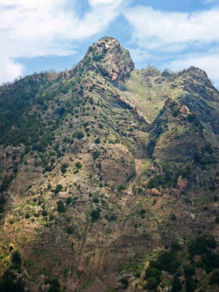 Rocky mountain slope with scattered vegetation under a partly cloudy sky