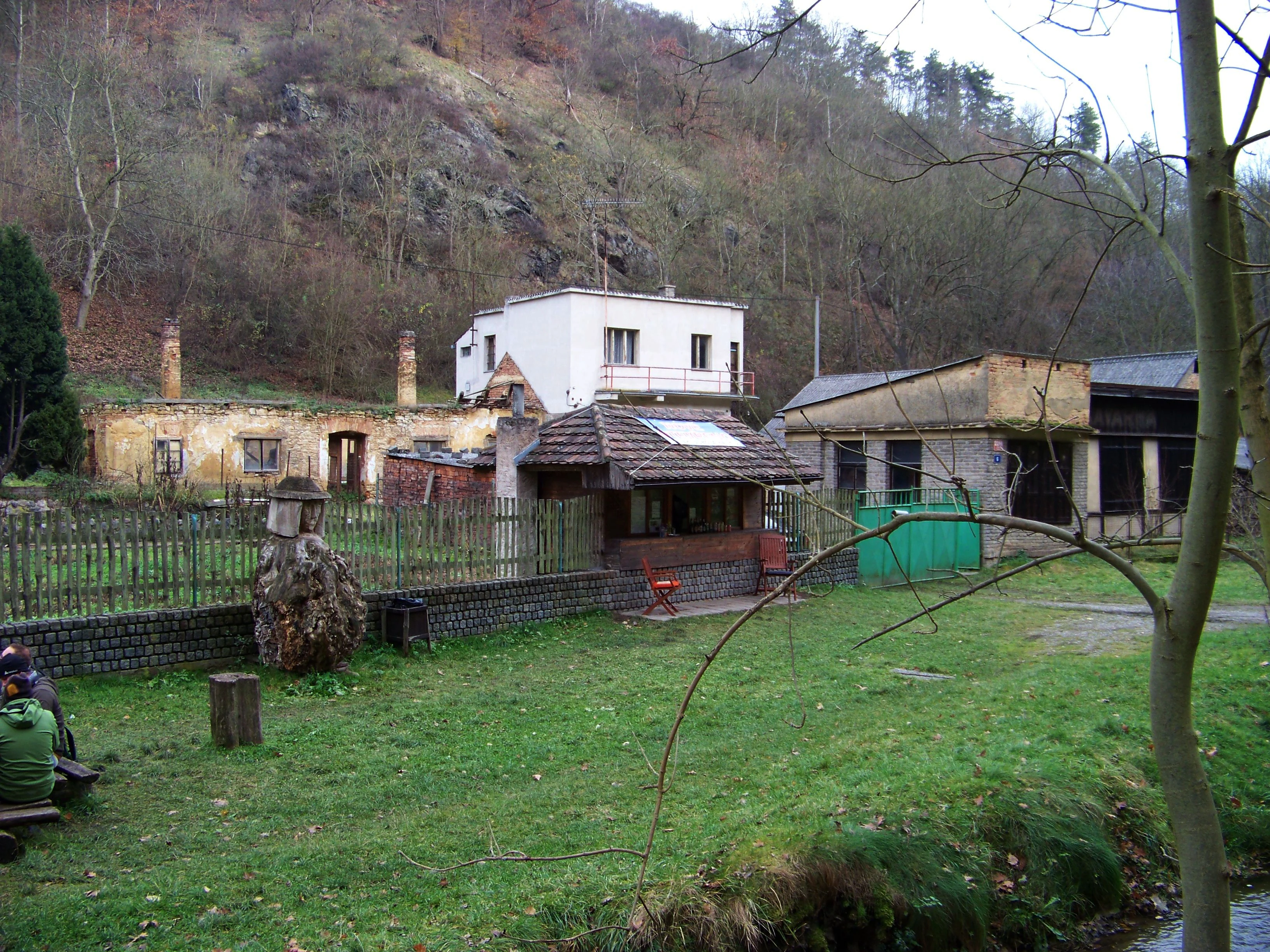 A view of low buildings and a small house set against a forested rocky hillside in the Ticha Sarka valley in Prague.