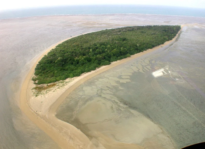 An aerial view of a low lying tropical island surrounded by expansive tidal sandflats and shallow reef environments.