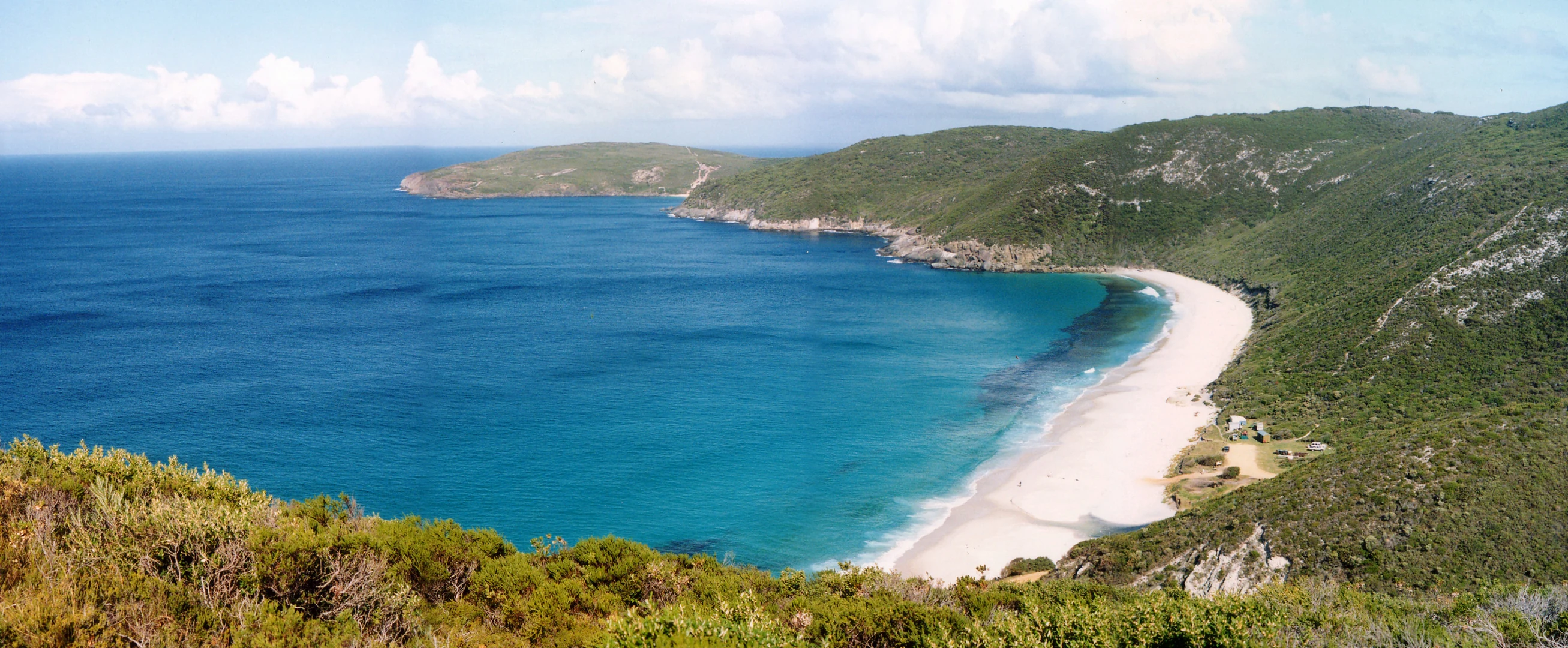 Coastal landscape with turquoise ocean, white sandy beach, green hills, and rocky headland