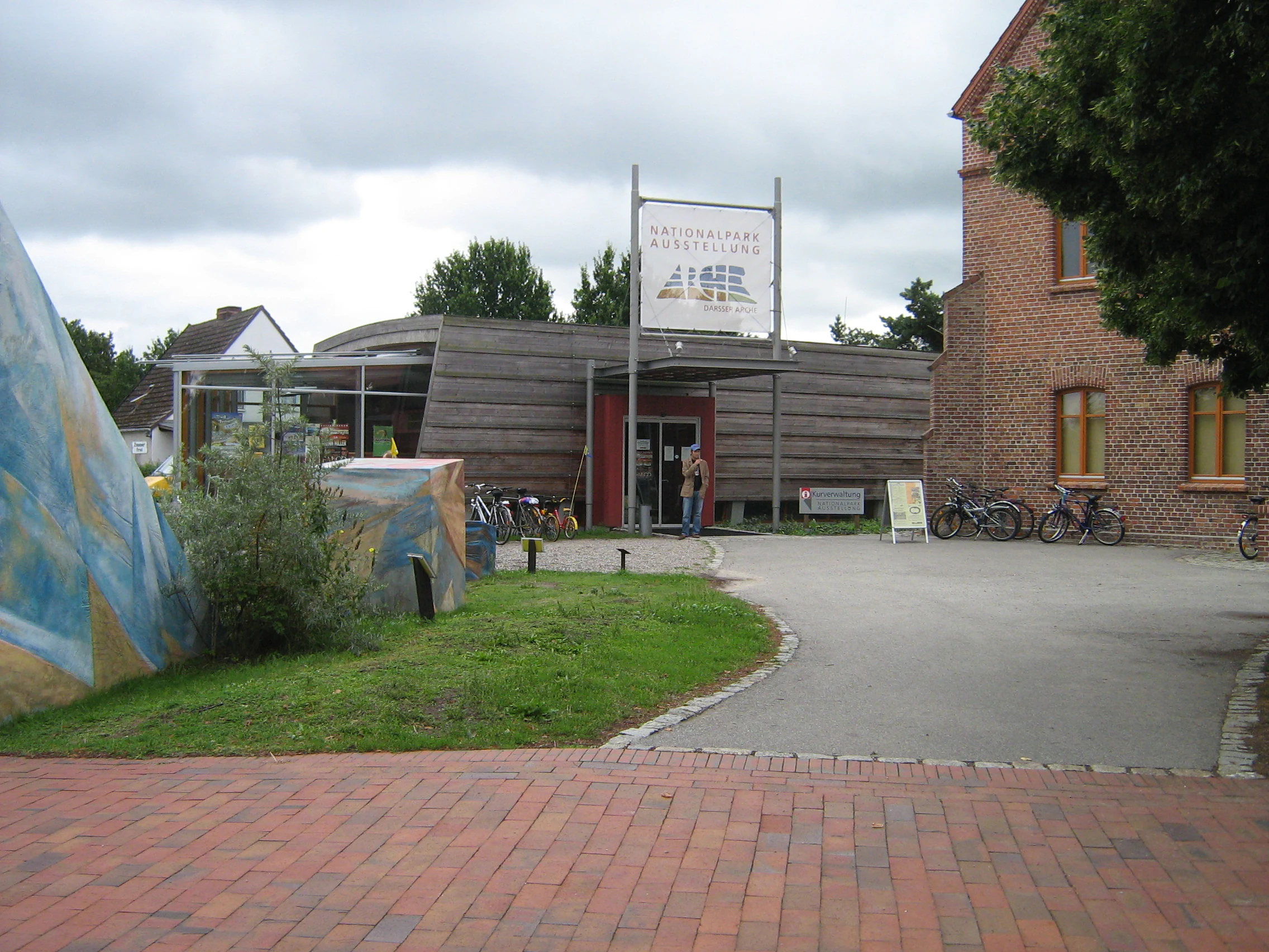 Brick building with 'National Park Museum Darsser Arche' sign, bicycles parked outside, grassy area, and paved pathway
