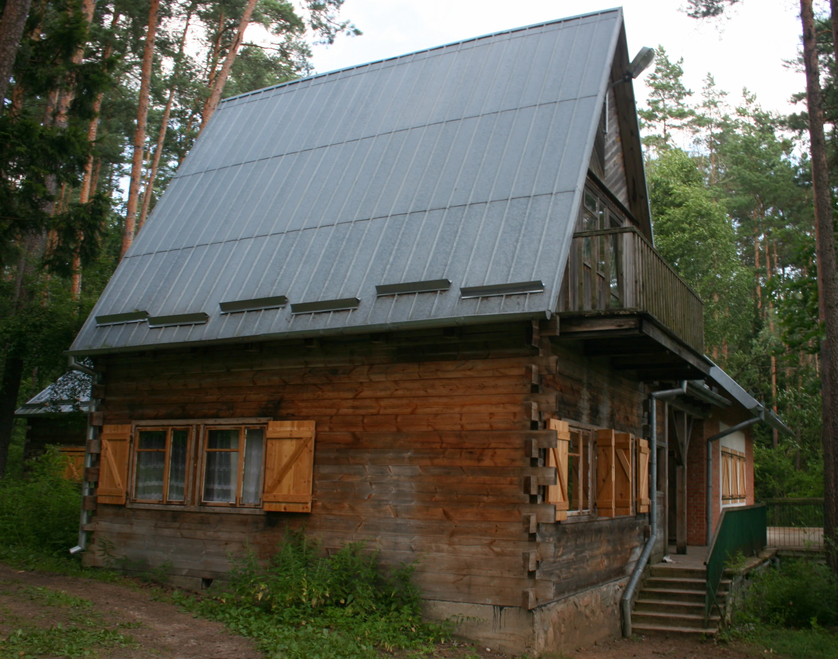 A rustic log cabin style building with a steep, silver-colored metal roof and wooden shutters, situated in a forest setting.