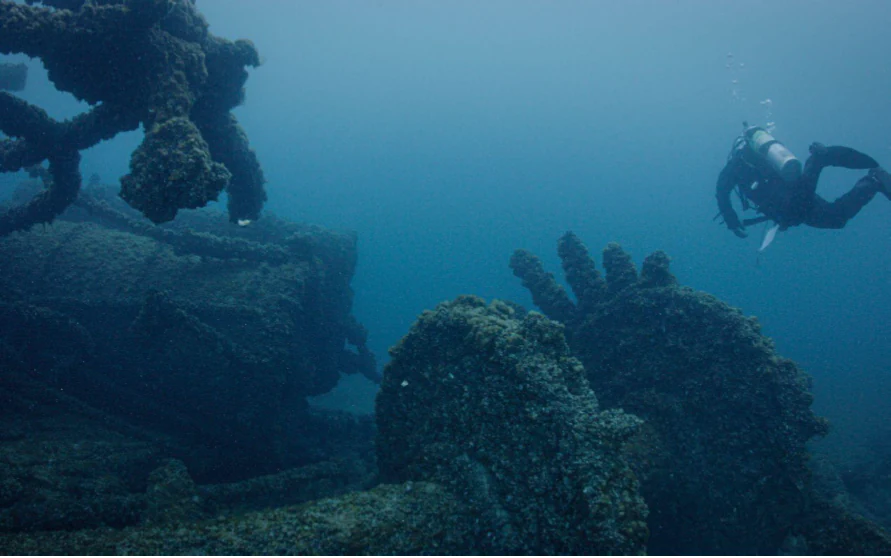 Un buceador nada cerca de la gran maquinaria sumergida y cubierta de percebes, y de los restos estructurales de un naufragio histórico bajo el agua en el lago Míchigan.