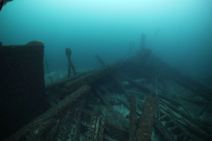 Vista submarina de la sección de proa en deterioro de un histórico naufragio de madera que descansa en el lecho del lago en aguas azules turbias.