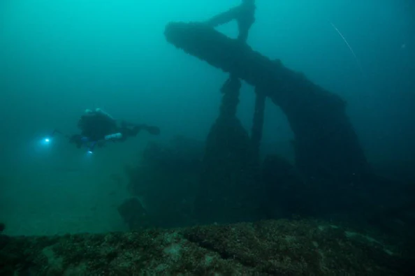 Un buceador con una luz subacuática brillante explora la oscura estructura sumergida de la popa de un naufragio en el lago Míchigan.