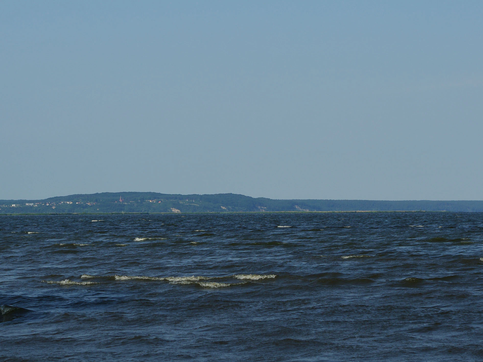 Wide view of the sea with distant shoreline and hills under a clear sky