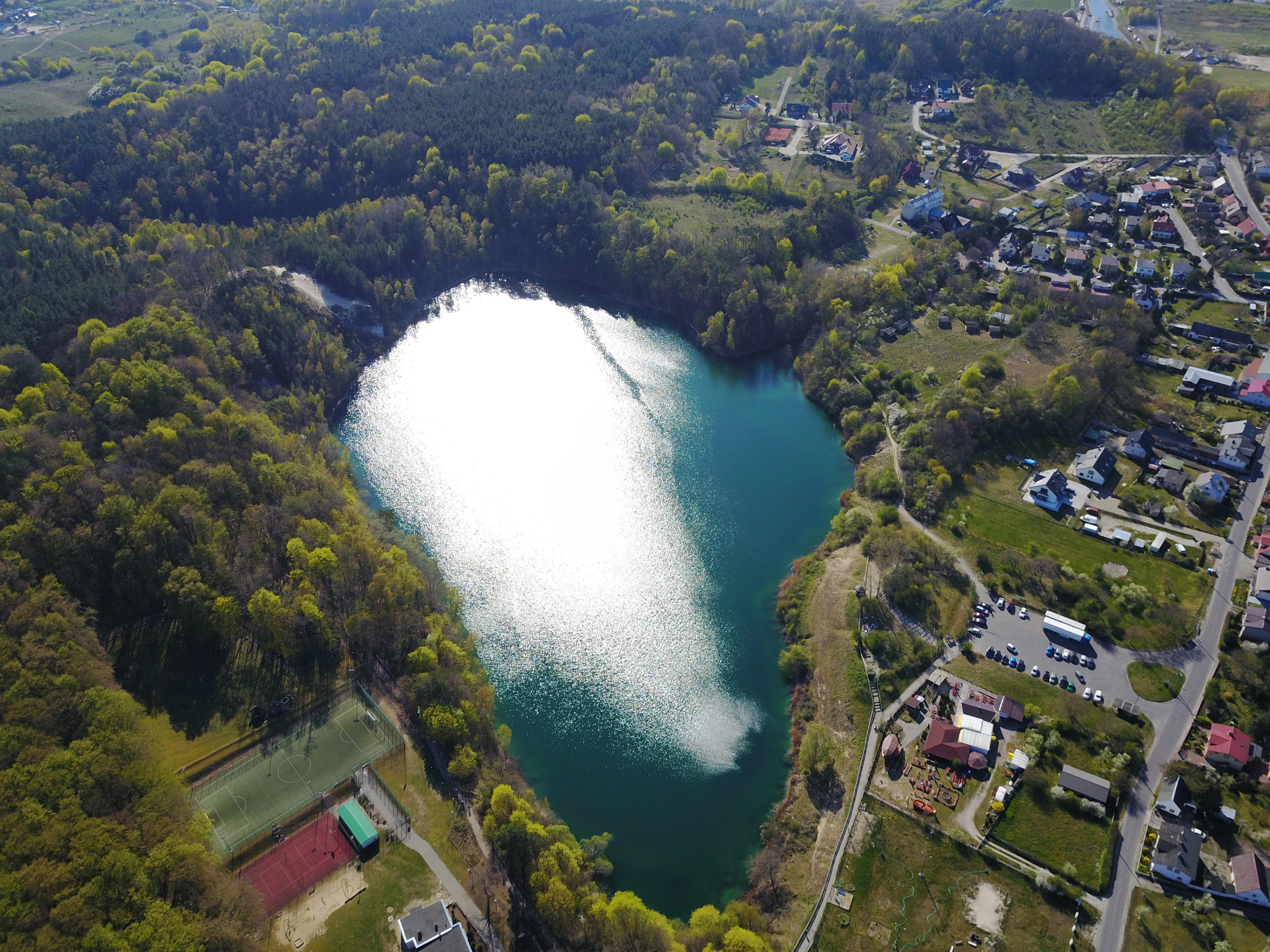 Aerial view of a bright turquoise lake surrounded by dense green forest and a small town area on the right bank.