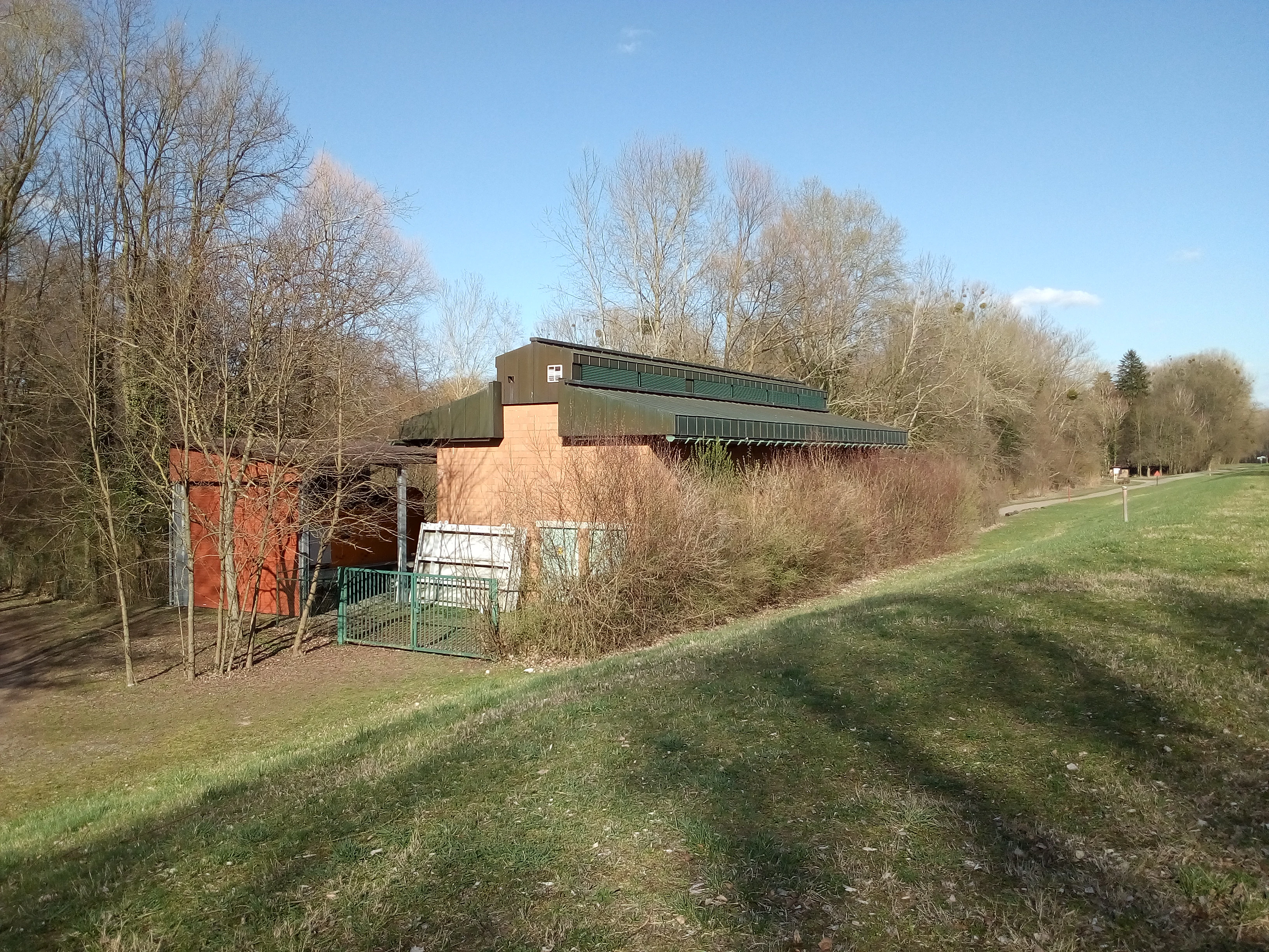 A brick pump station building with a green roof set near trees and a grassy embankment.