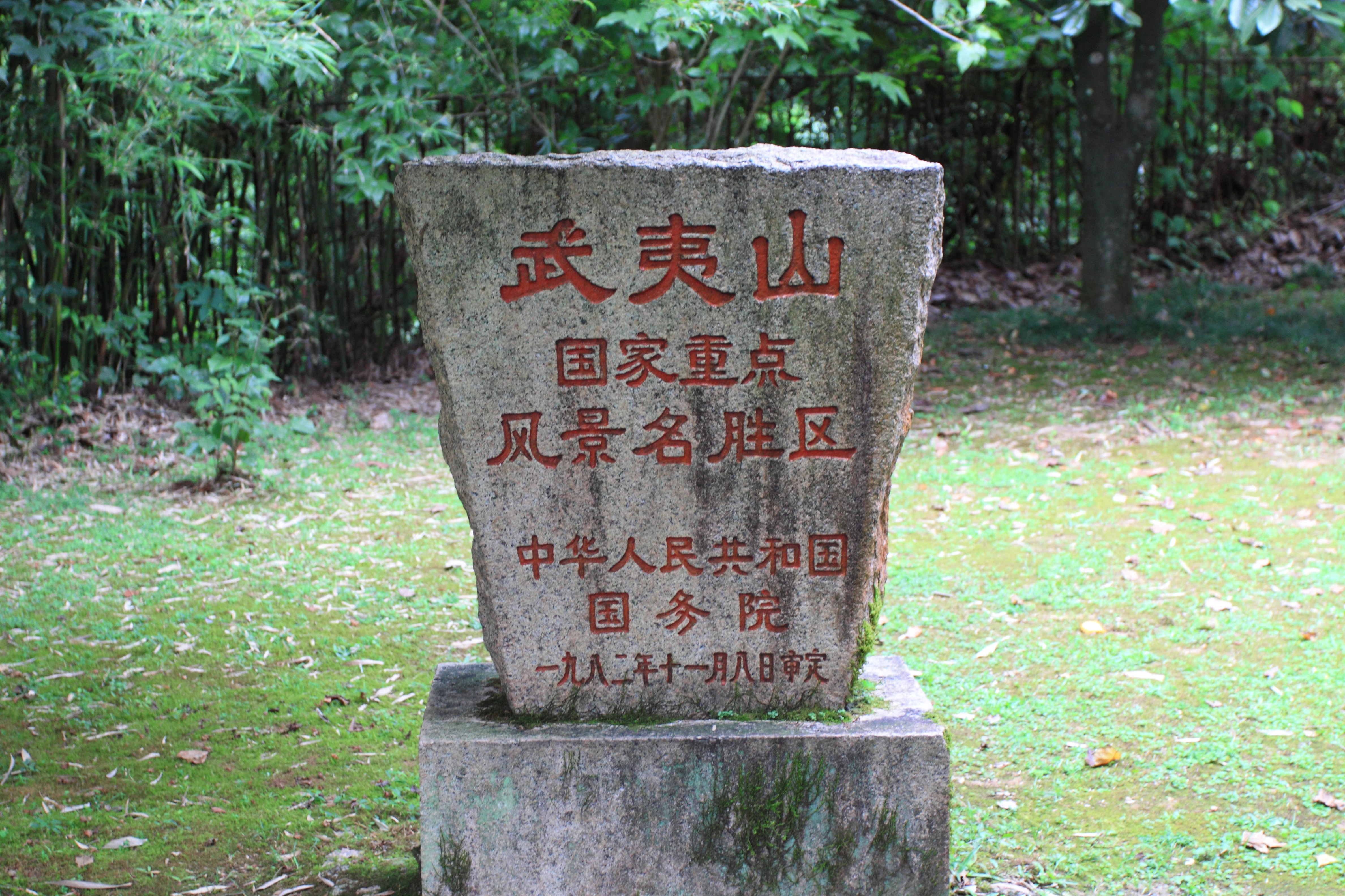 A weathered stone monument featuring red-painted Chinese characters set in a lush, green outdoor area.