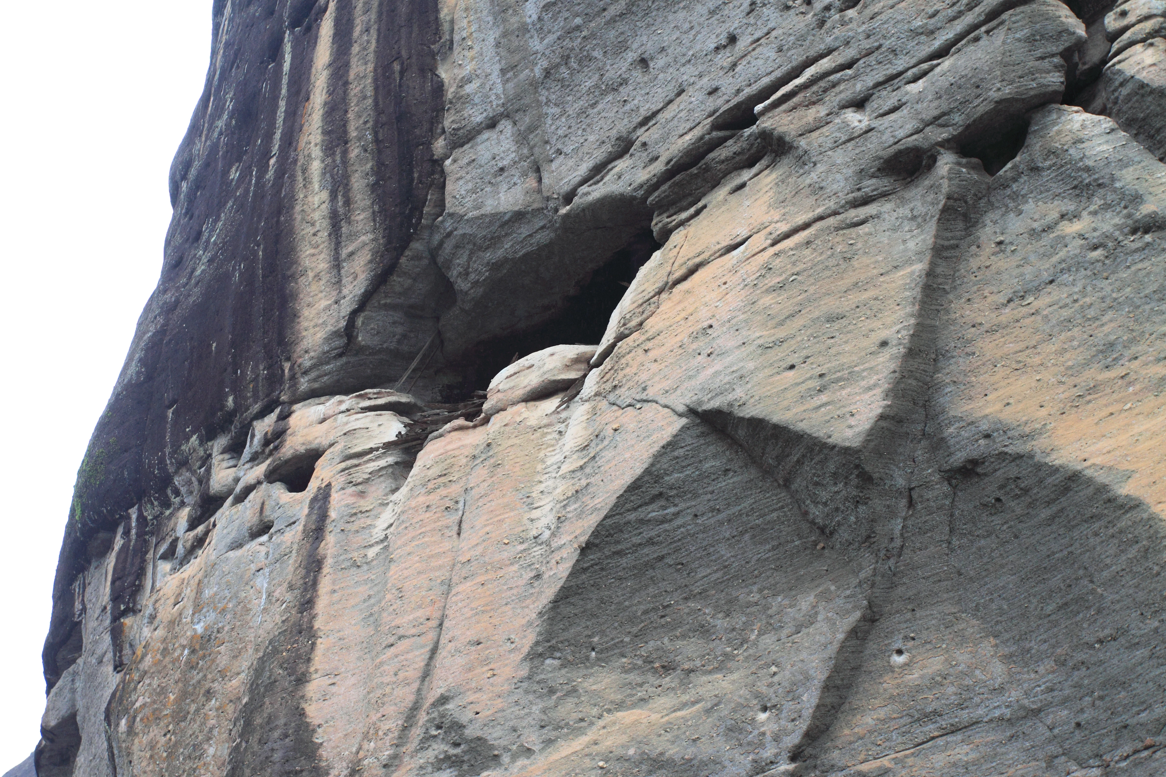A steep, weathered cliff face composed of layered rock, with a shadowed recess suggesting the location of an ancient tomb.