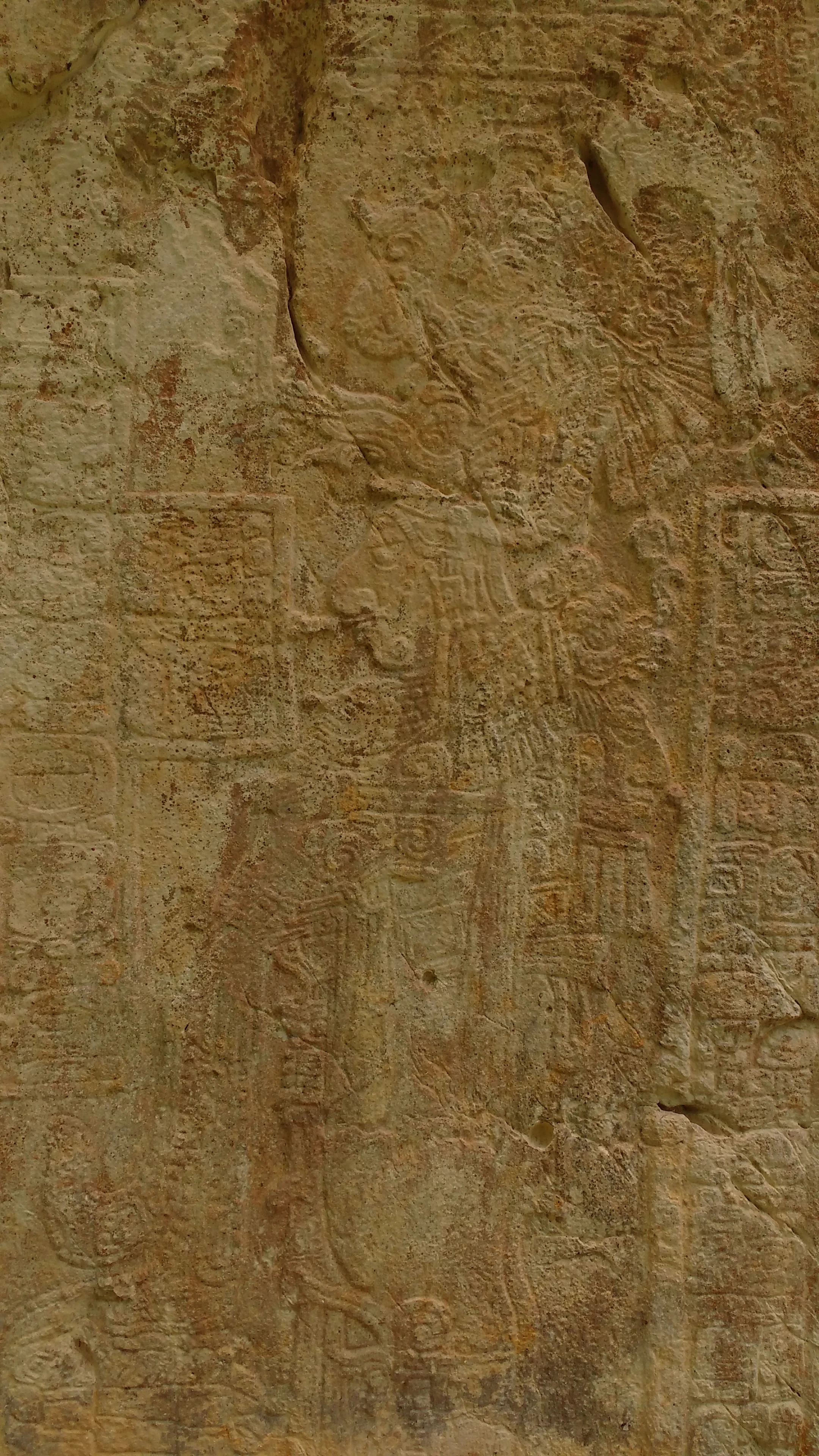Close up view of an ancient Maya limestone relief carving depicting human figures and hieroglyphs on a weathered, tan colored stone surface.