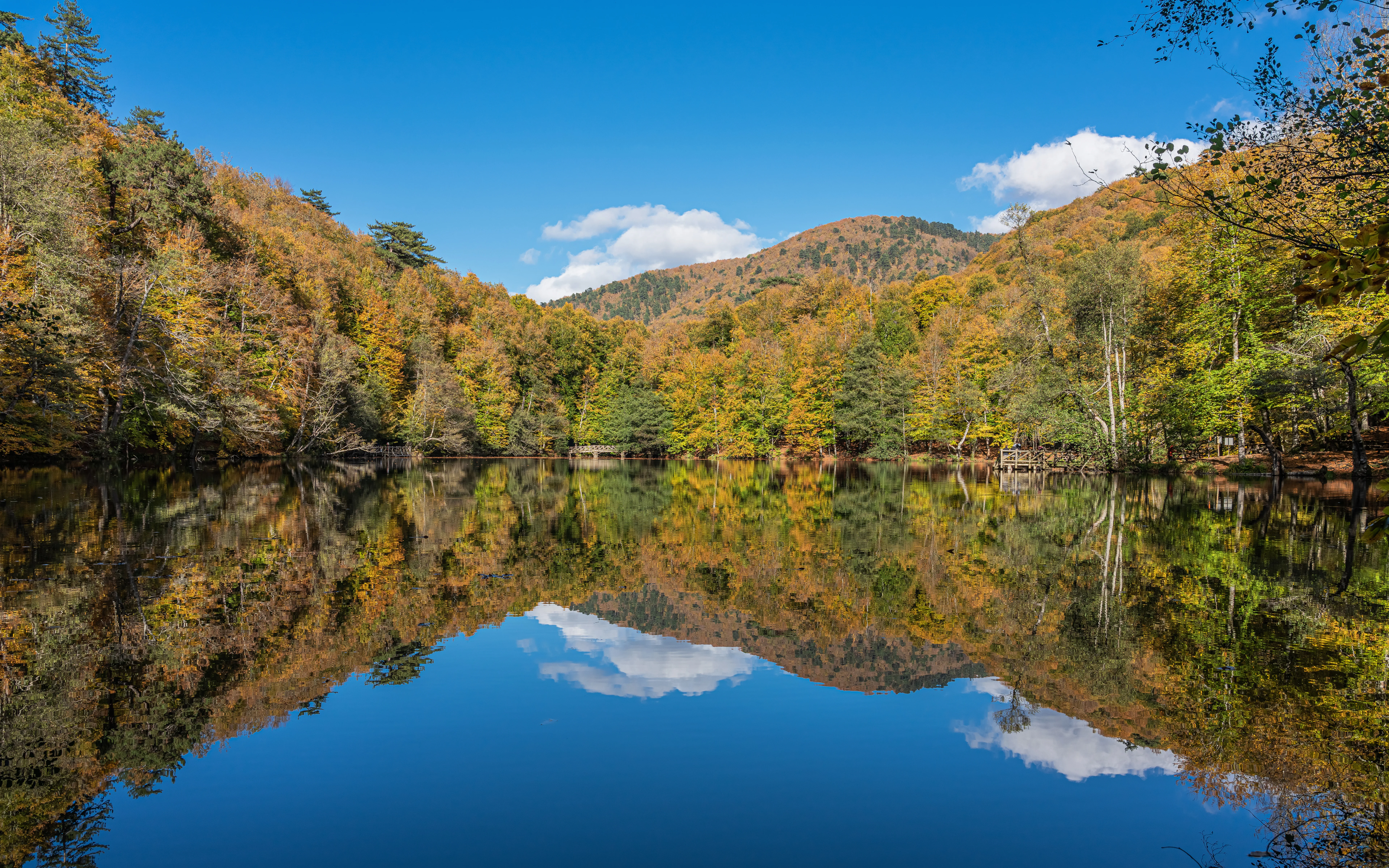 A lake reflecting mountains and autumn-colored trees under a clear blue sky.