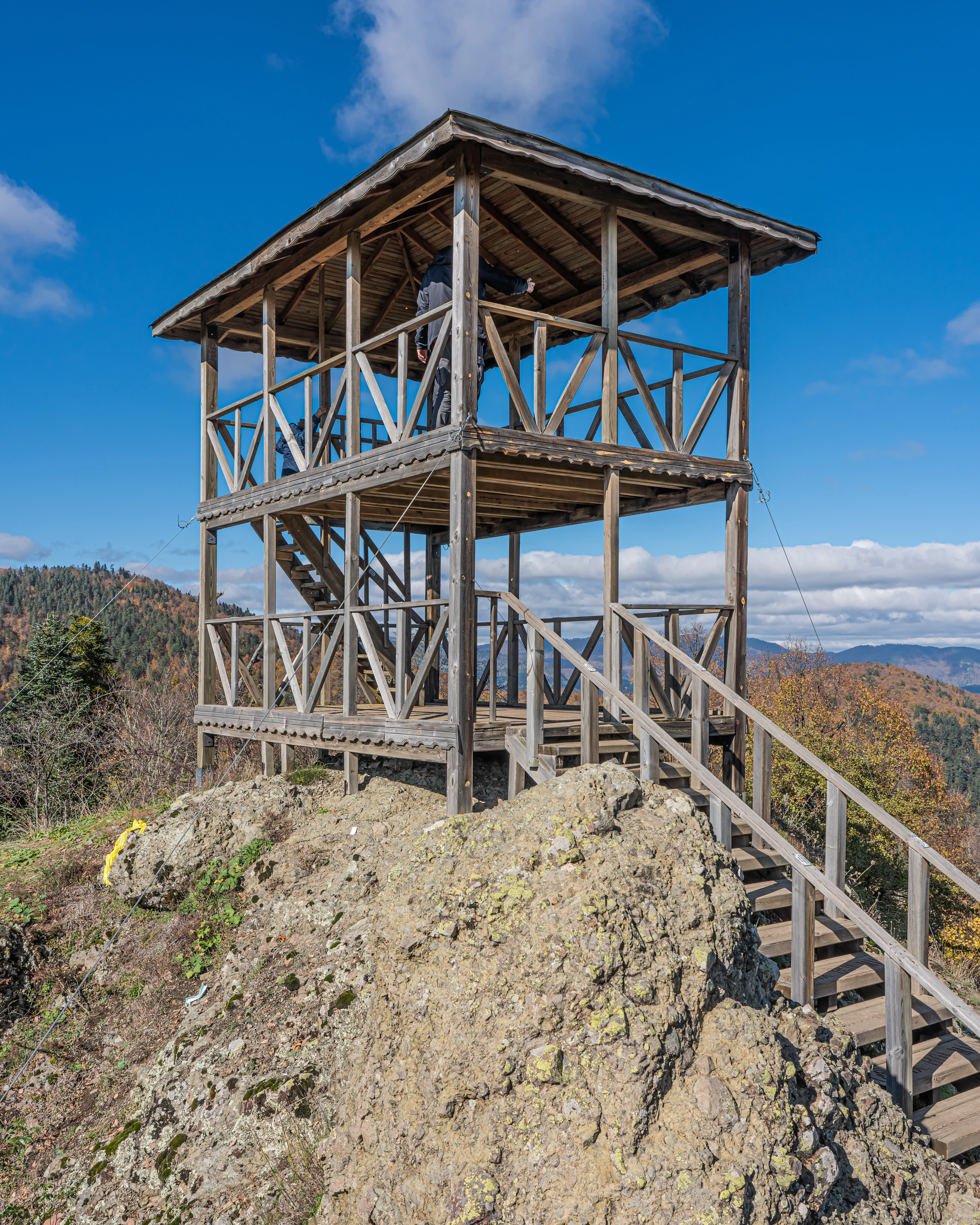 Wooden two-story observation tower on rocky terrain with mountain landscape in background