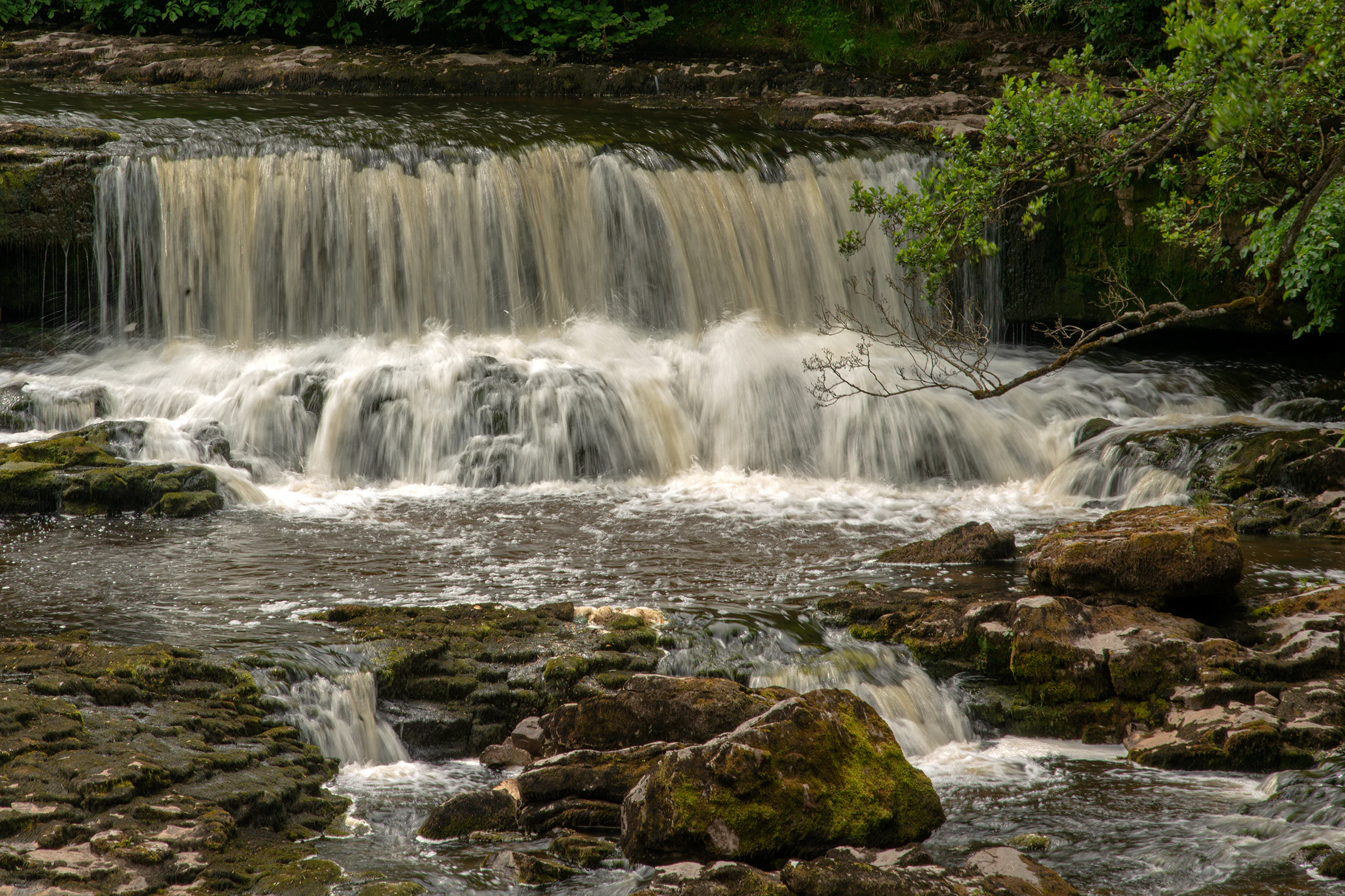 Waterfall with multiple tiers flowing over moss-covered rocks surrounded by green foliage