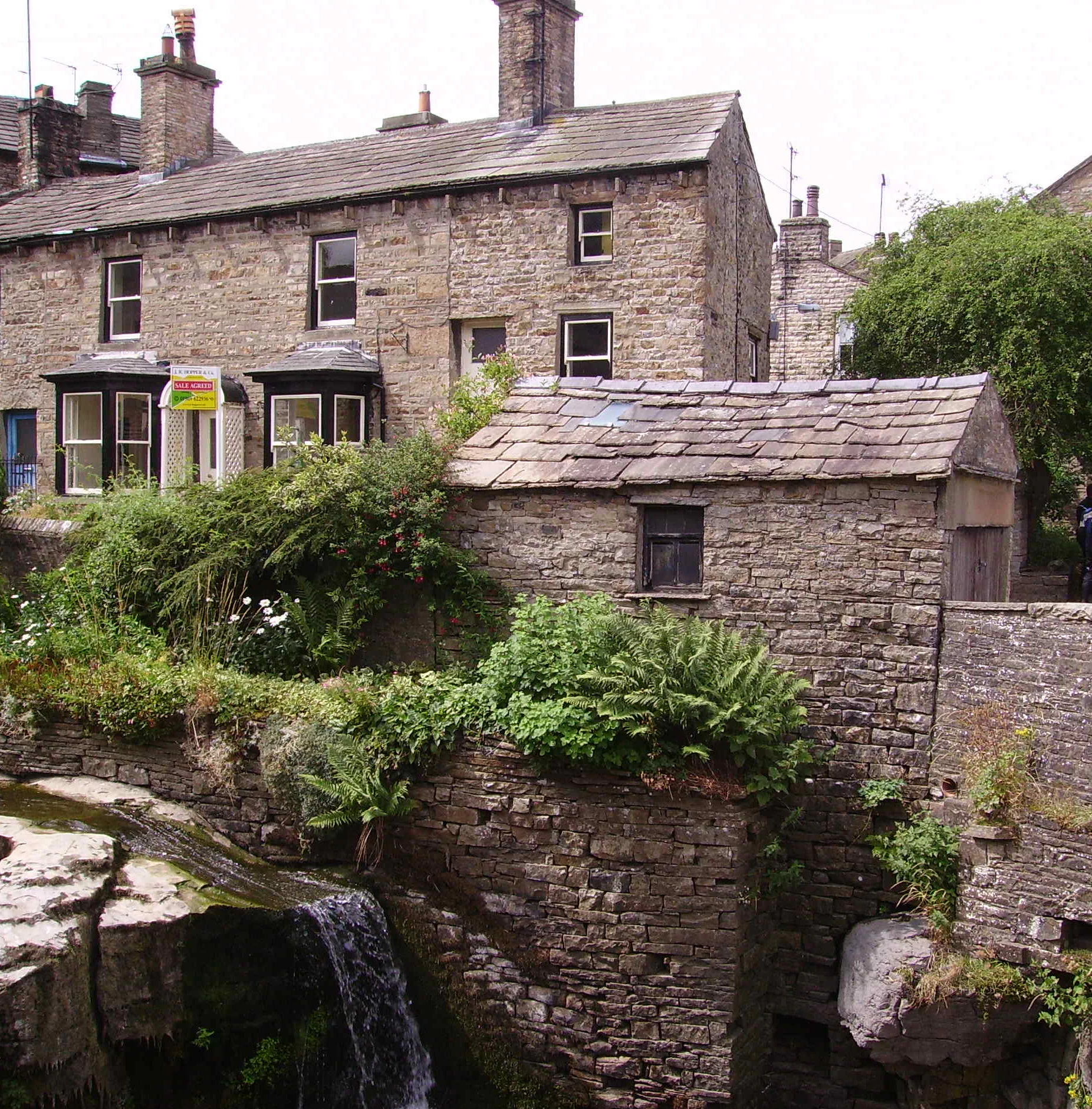 Stone houses with slate roofs and a small waterfall flowing over stone walls in Hawes village